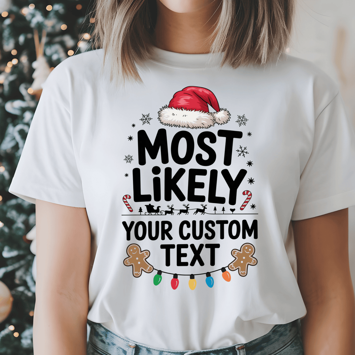 A woman wearing a white graphic t-shirt with a Christmas design that reads 'MOST LIKELY YOUR CUSTOM TEXT' with a Santa hat, gingerbread cookies, candy canes, and lights. The background shows a blurred Christmas tree.