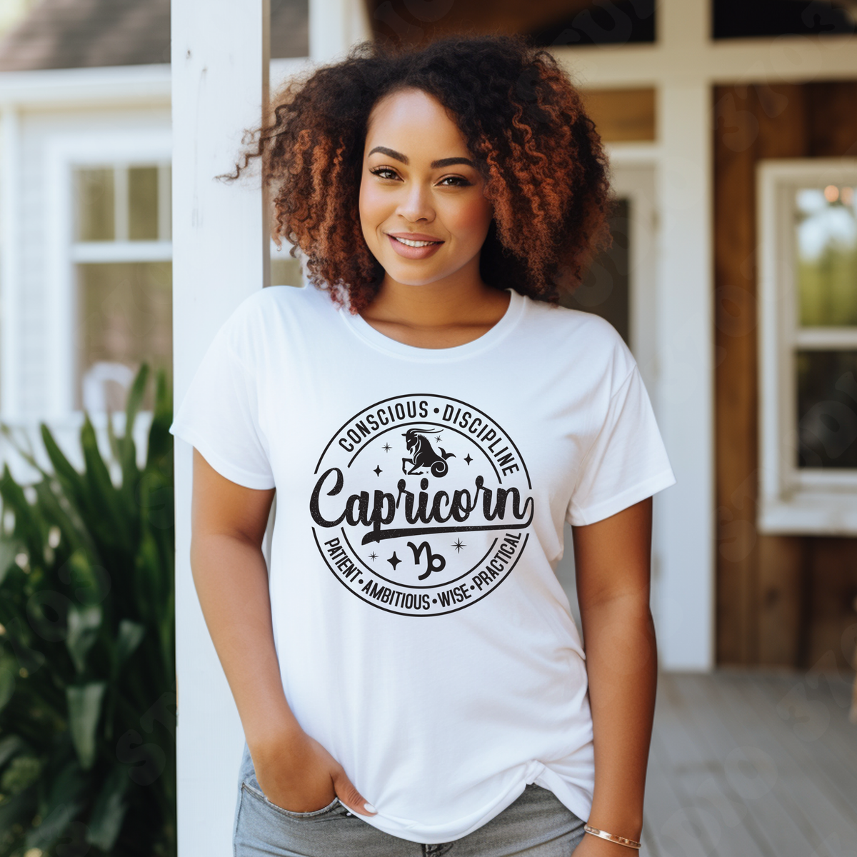 A woman with curly brown hair stands on a porch wearing a white graphic T-shirt with a black circular design that reads 'Virgo' and lists adjectives around it. The background shows a home exterior with white columns, wood siding, and green plants.