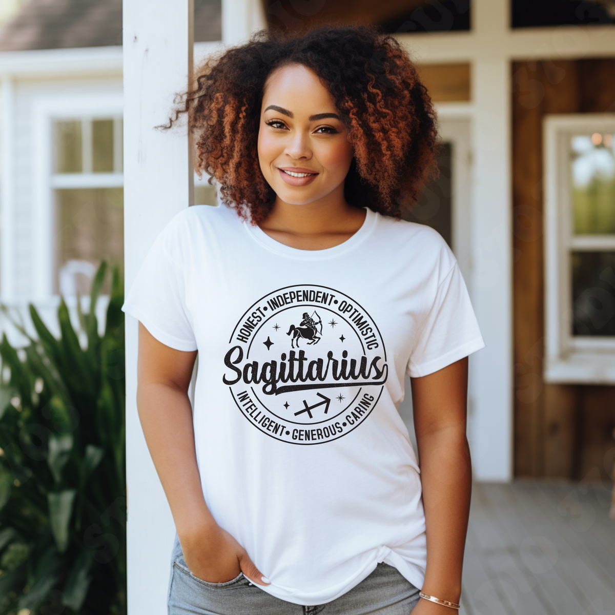 A woman with curly brown hair stands on a porch wearing a white graphic T-shirt with a black circular design that reads 'Virgo' and lists adjectives around it. The background shows a home exterior with white columns, wood siding, and green plants.