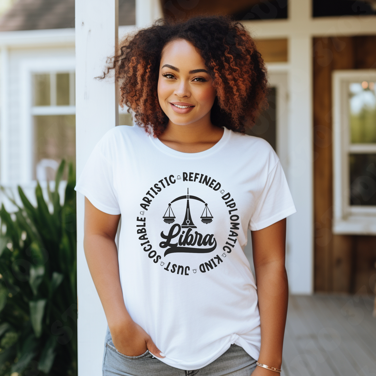 Woman wearing a white crewneck t-shirt featuring a black circular Libra zodiac graphic with a scales illustration, the word "Libra," and trait keywords like artistic, refined, diplomatic, kind, just, and sociable.