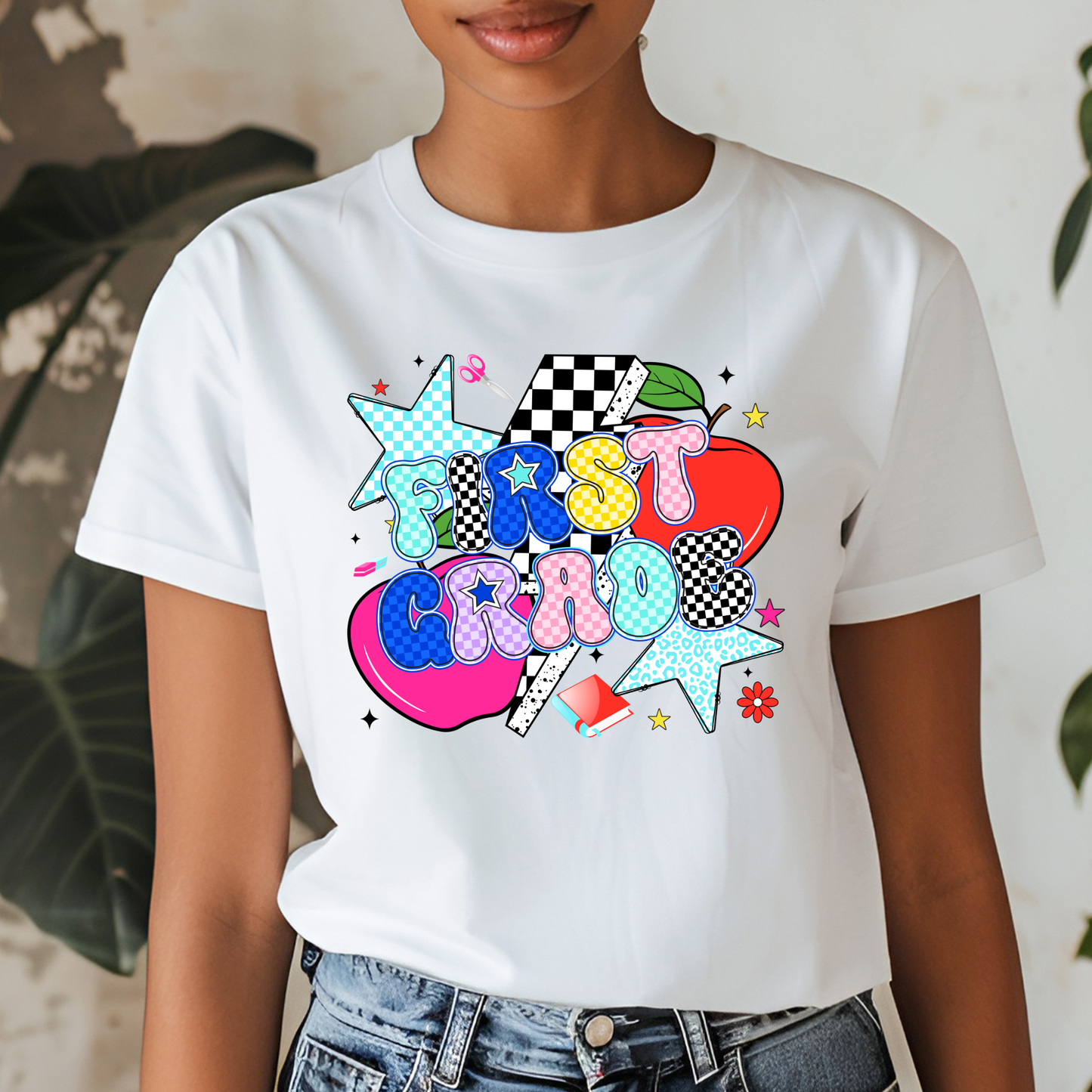 A woman wearing a white short-sleeve graphic t-shirt with a colorful retro-style 'FIRST CLASS' design featuring stars, apples, and checkered patterns, paired with blue jeans.