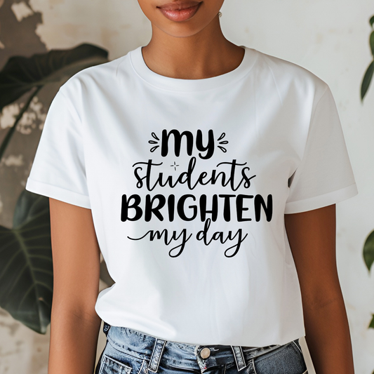 A woman wearing a white short-sleeve graphic T-shirt with the black text 'my students BRIGHTEN my day' printed on the front, paired with blue jeans.