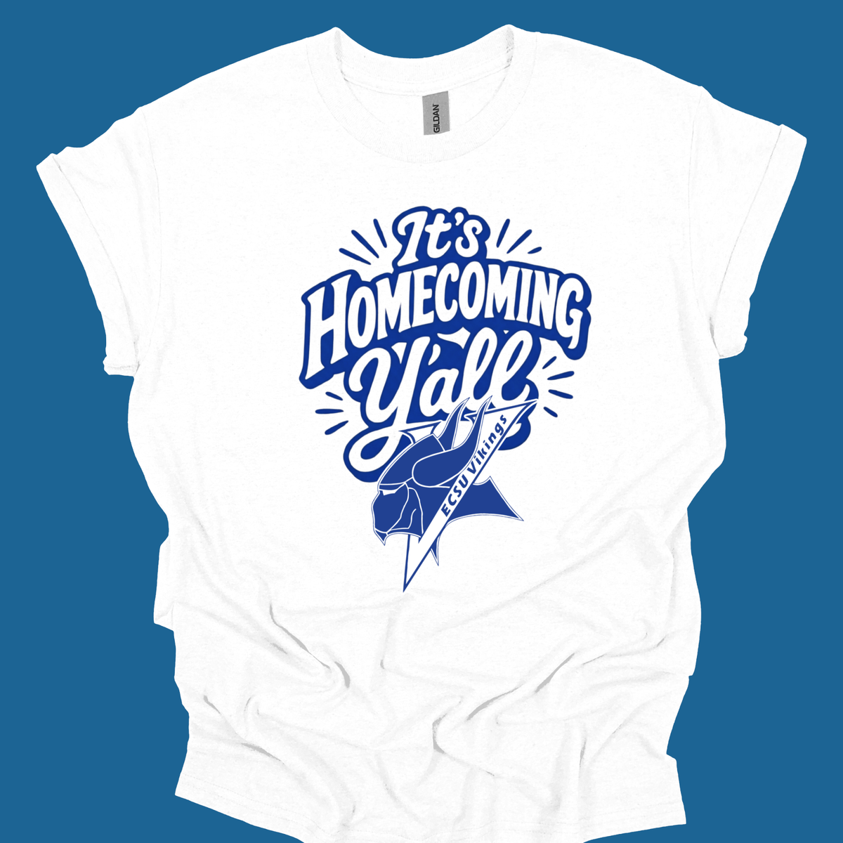 A white short-sleeve t-shirt with a blue graphic that reads 'It's Homecoming Yell' above a blue mascot silhouette, shown against a solid blue background.