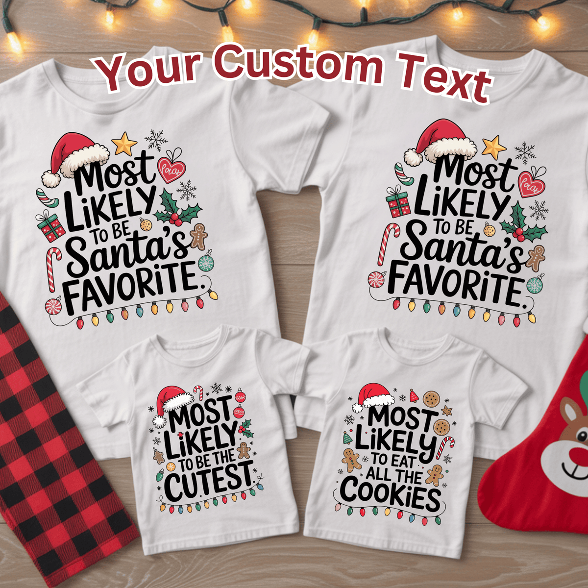 Three white Christmas family T-shirts arranged on a wood surface with holiday props. The shirts feature black text with festive illustrations: the large shirts say 'Most Likely to be Santa's Favorite' and the smaller shirts say 'Most Likely to be the Cutest' or 'Most Likely to eat all the Cookies.