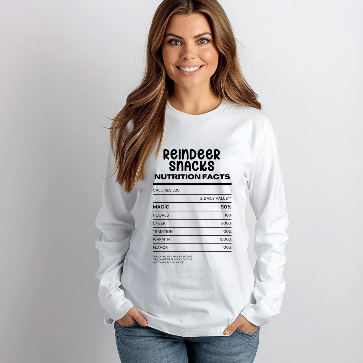 A woman wearing a white long-sleeve t-shirt with a black graphic print styled like a nutrition facts label reading 'Reindeer Snacks Nutrition Facts'.