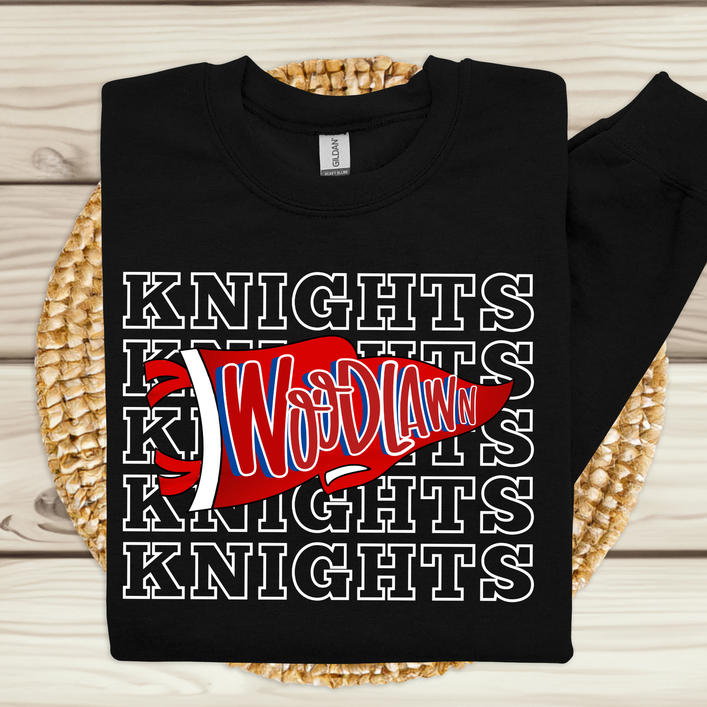 A black long-sleeve t-shirt with a 'Knights Wodlaw' graphic, laid flat on a woven straw mat over a light wood plank background.