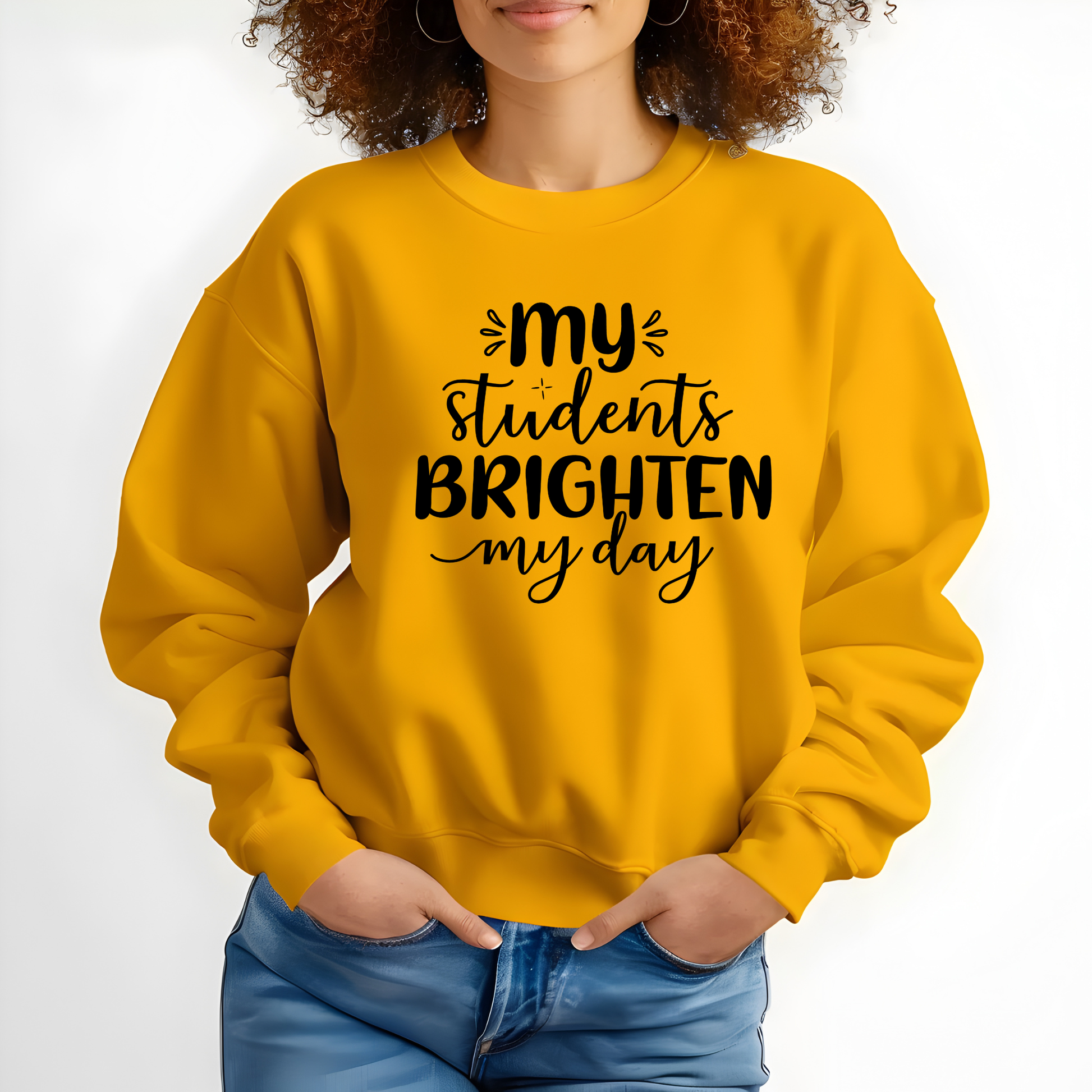 A woman wearing a bright yellow crewneck sweatshirt with the black printed text 'my students BRIGHTEN my day' on the front, paired with blue jeans against a plain white background.