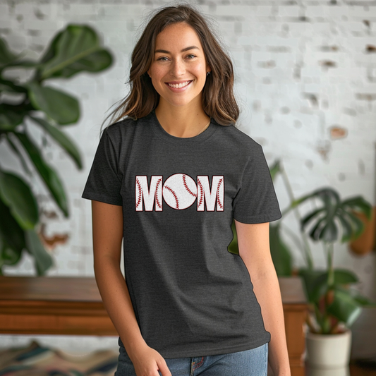 Woman wearing a dark gray t-shirt with 'MOM' printed on it, standing in a room with plants and a brick wall.