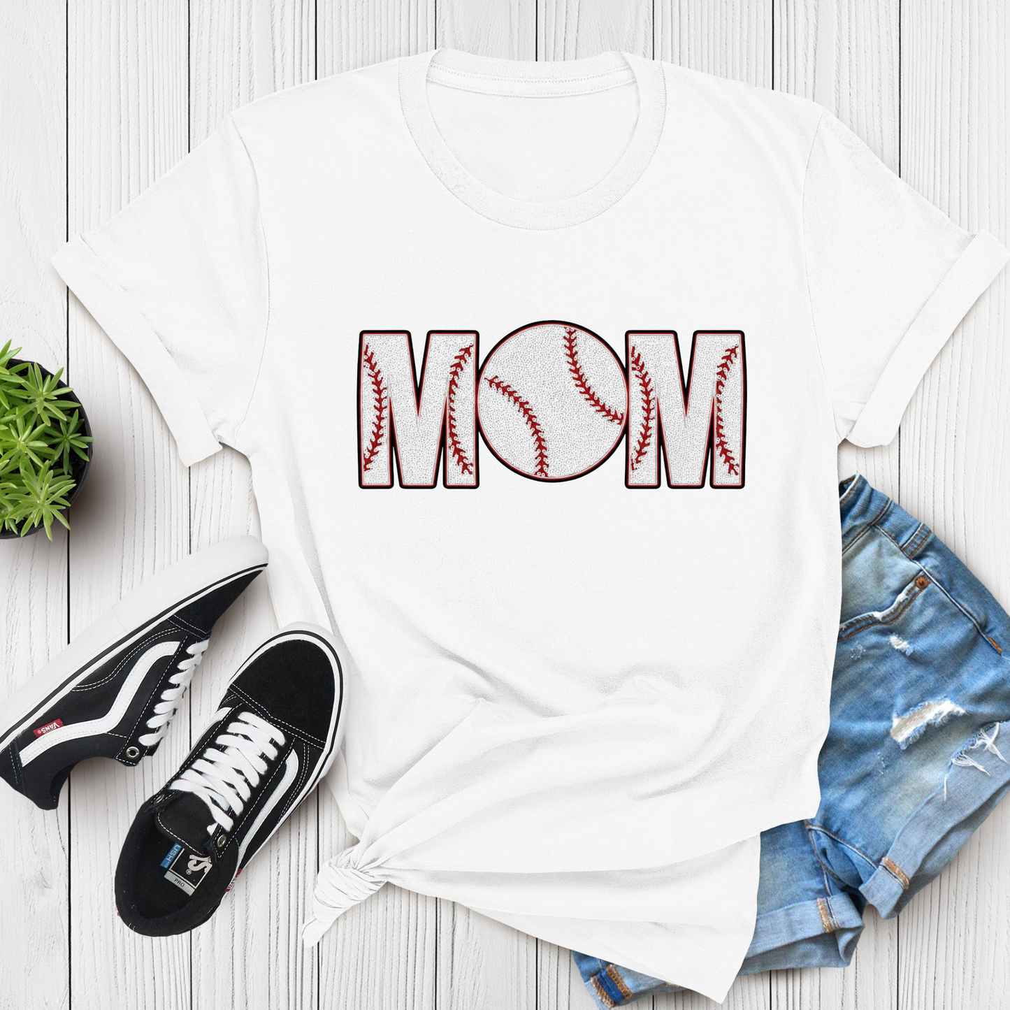 White t-shirt with 'Mom' design, black sneakers, and denim shorts on a wooden surface.