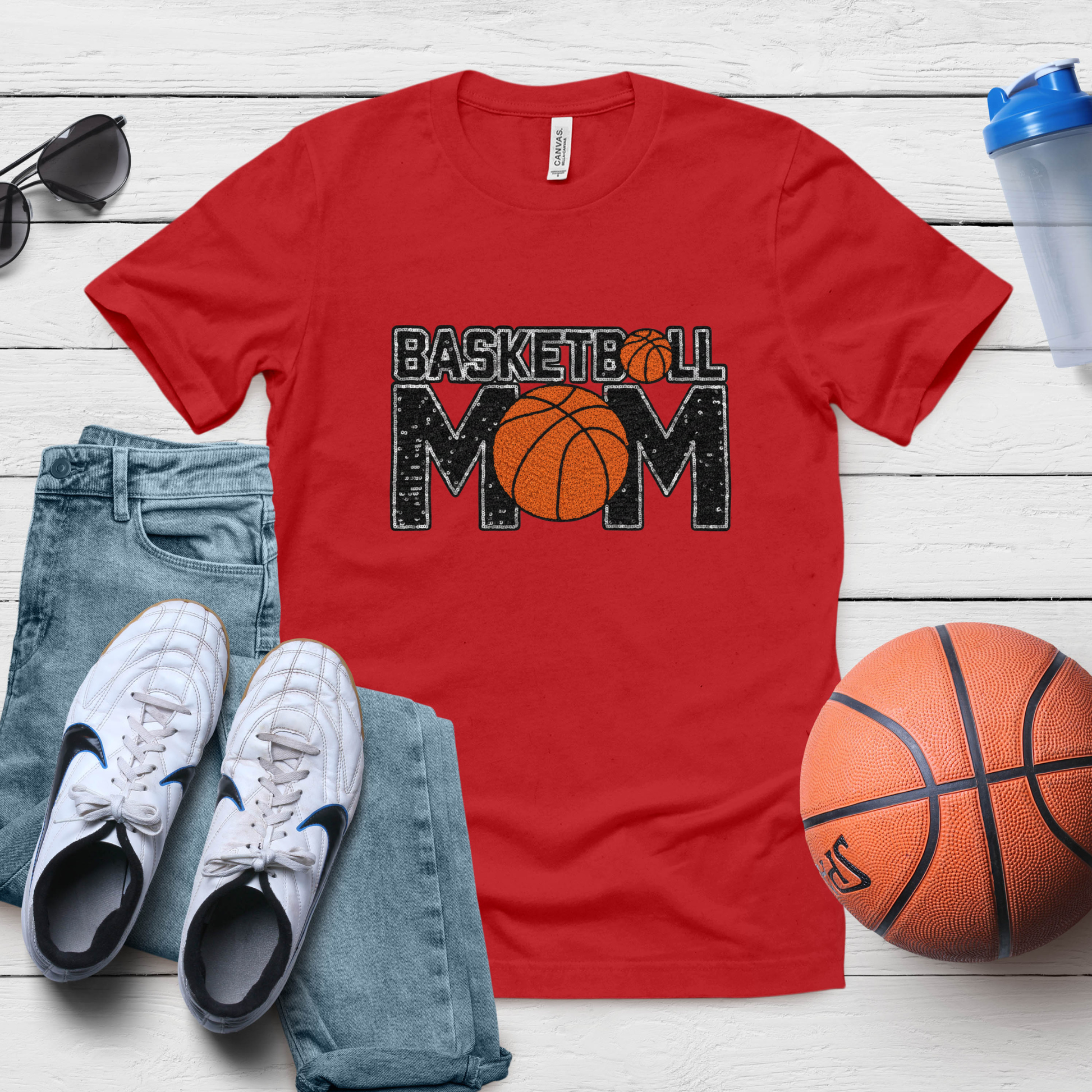 Red t-shirt with 'Basketball Mom' design, paired with jeans, sneakers, and a basketball on a wooden surface.