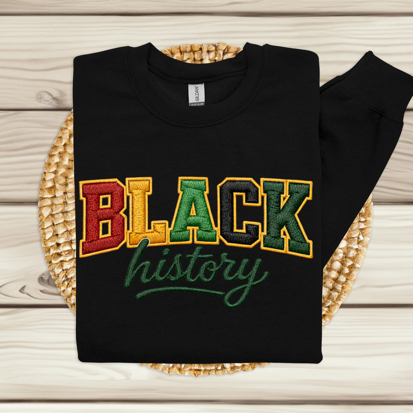 Black sweatshirt with 'BLACK history' text in multicolor on a woven mat.