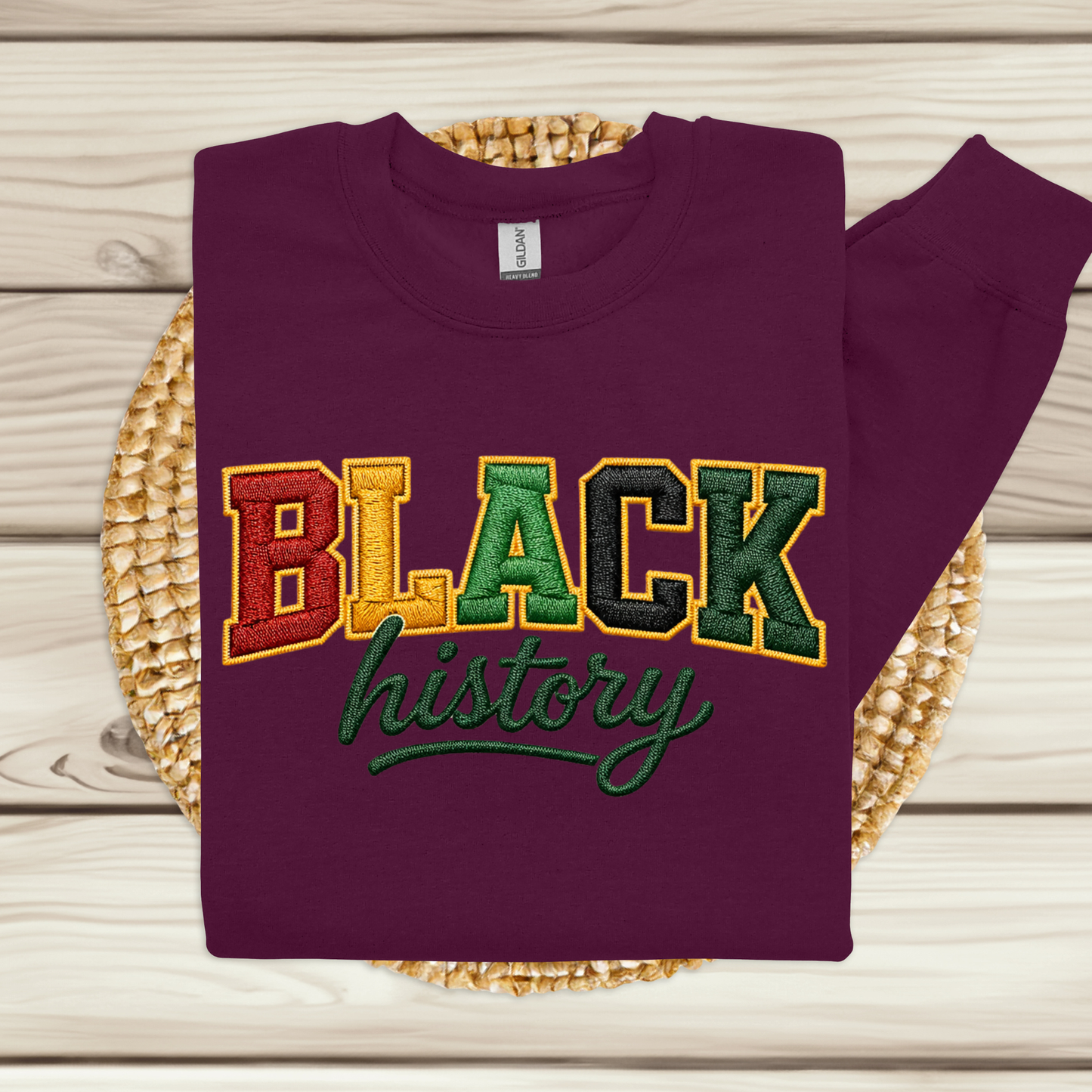 Folded purple sweatshirt with 'BLACK history' text in multicolor on a wooden surface