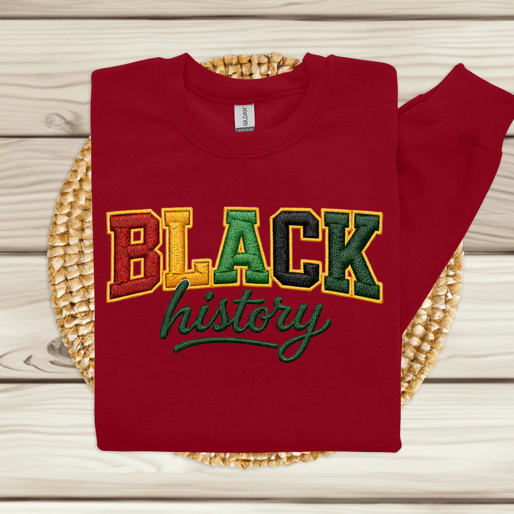 Red sweatshirt with 'BLACK history' text in multicolor on a woven mat.