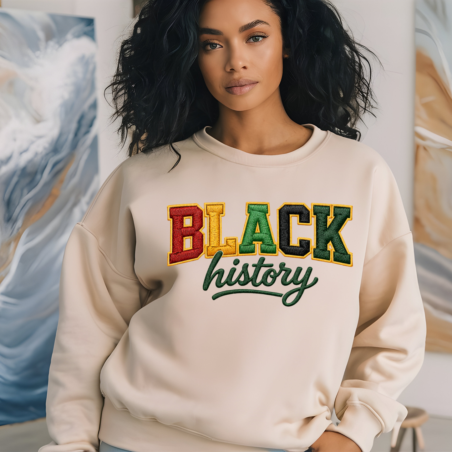 Person wearing a beige sweatshirt with 'BLACK history' text in multicolors against a colorful abstract painting background.