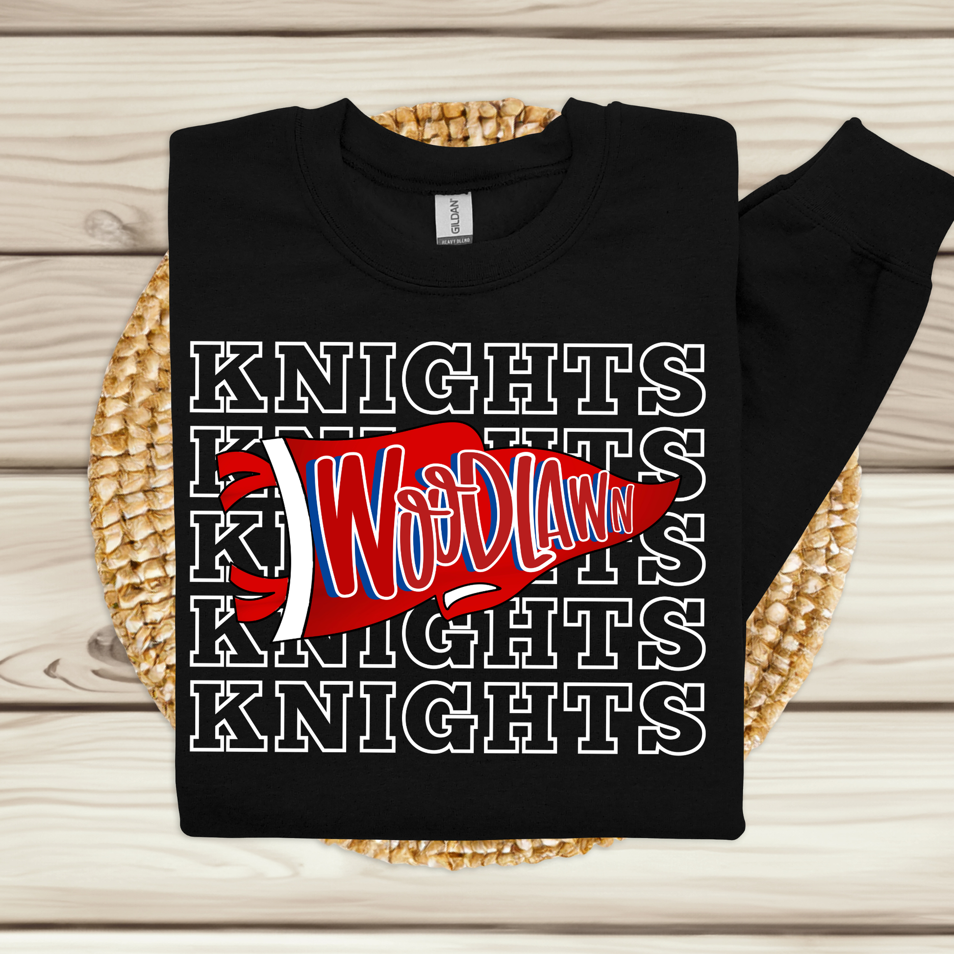 A black long-sleeve sweatshirt laid flat on a woven round mat over a light wood plank surface. The sweatshirt has a large front graphic with repeated outlined 'KNIGHTS' text in white, a red pennant shape, and stylized white and blue lettering reading 'Wood Law'.