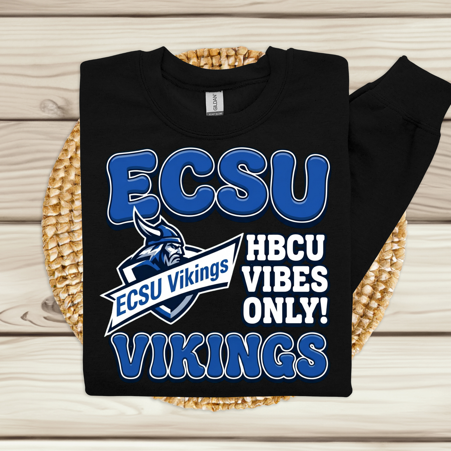 A black long-sleeve sweatshirt with a blue and white ECSU Vikings graphic, displayed flat on a woven placemat over a light wood background.