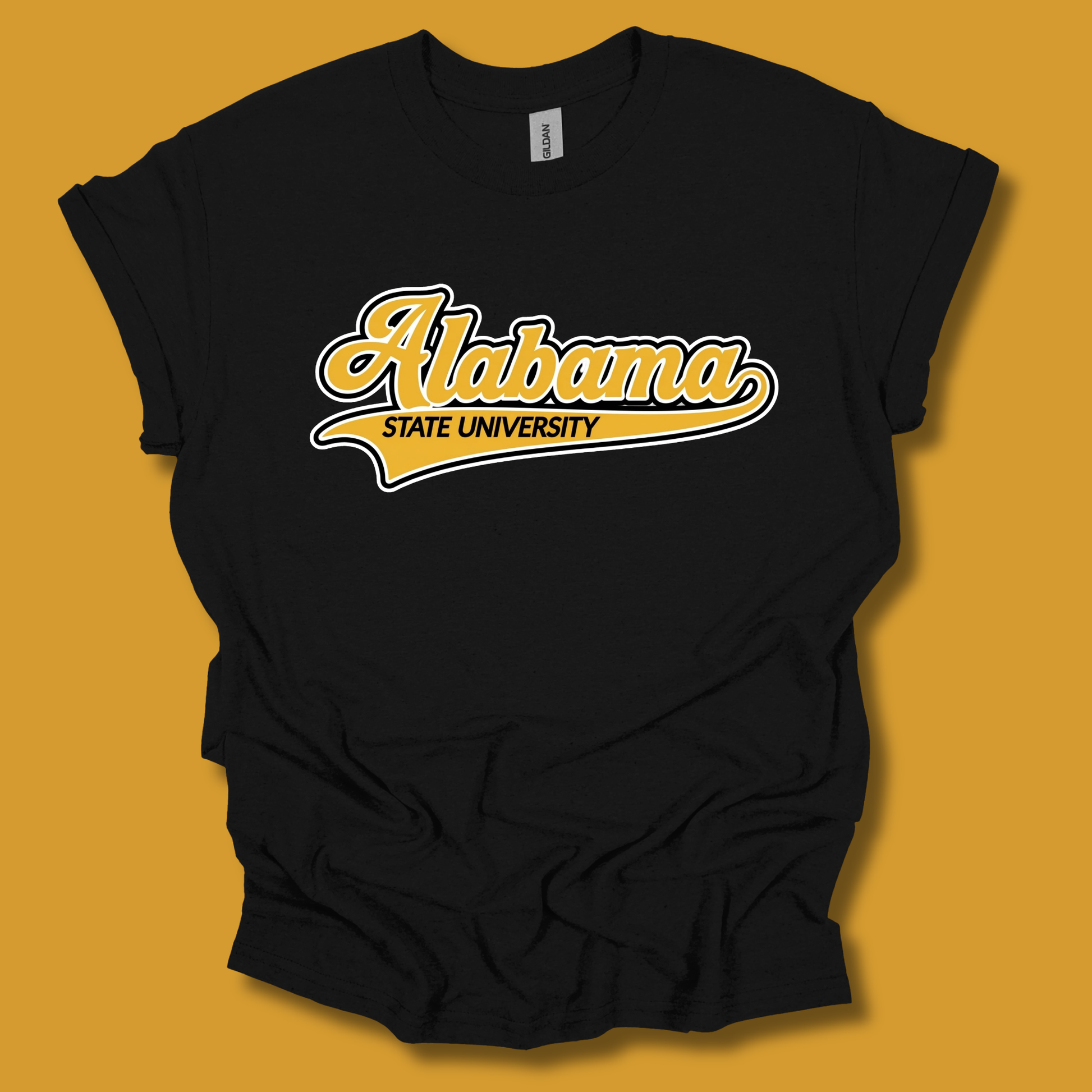 A black short-sleeve t-shirt with a yellow and white 'Alabama State University' graphic on the chest, displayed against a solid mustard yellow background.