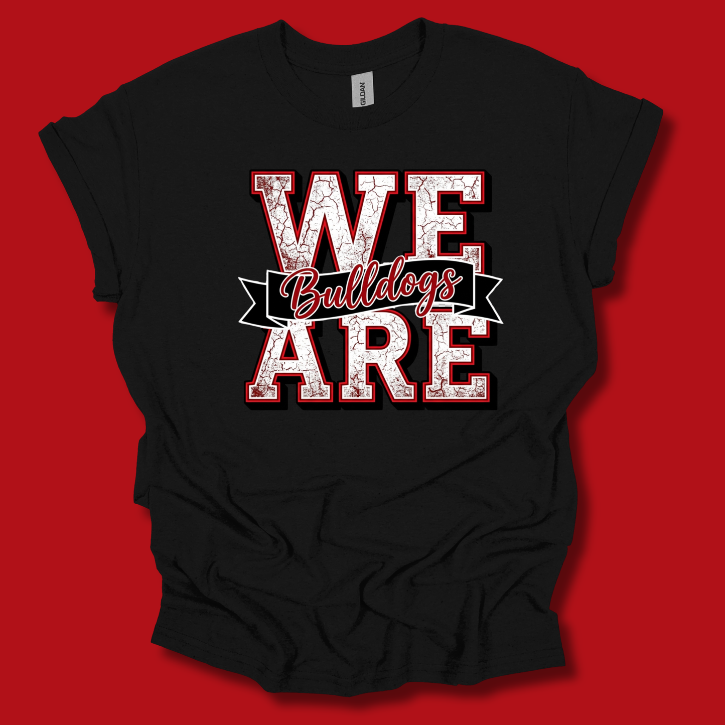 A black short-sleeve t-shirt with a distressed graphic reading 'WE ARE Bulldogs' in red and white, laid flat against a solid red background.