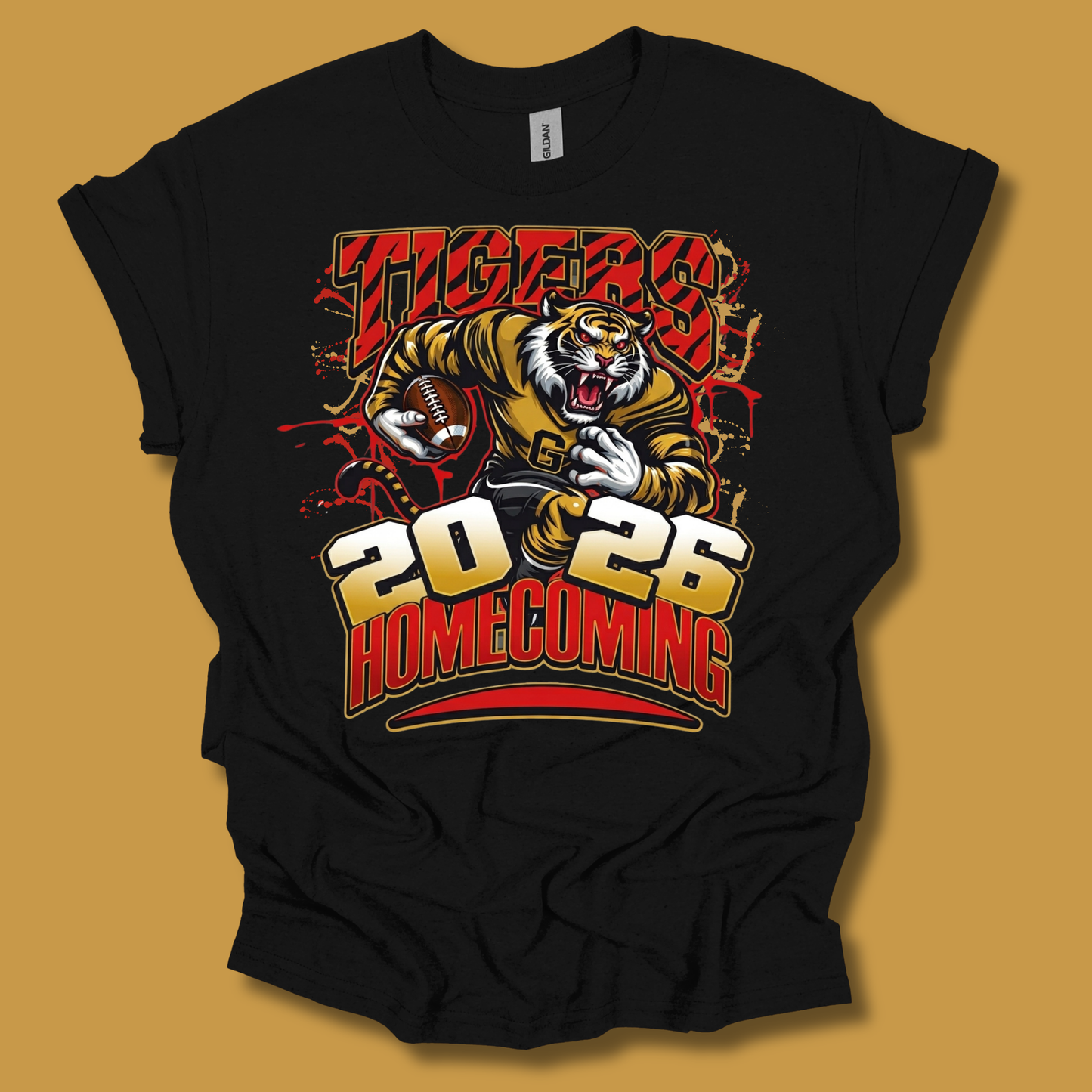 A black short-sleeve graphic t-shirt featuring a tiger mascot holding a football with 'TIGERS 2026 HOMECOMING' printed in bold red, gold, and white lettering. The t-shirt is displayed flat against a solid mustard yellow background.