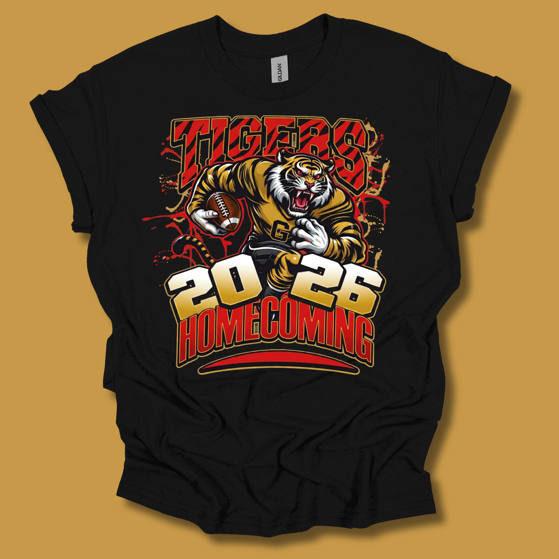A black short-sleeve graphic t-shirt featuring a tiger mascot holding a football with 'TIGERS 2026 HOMECOMING' printed in bold red, gold, and white lettering. The t-shirt is displayed flat against a solid mustard yellow background.