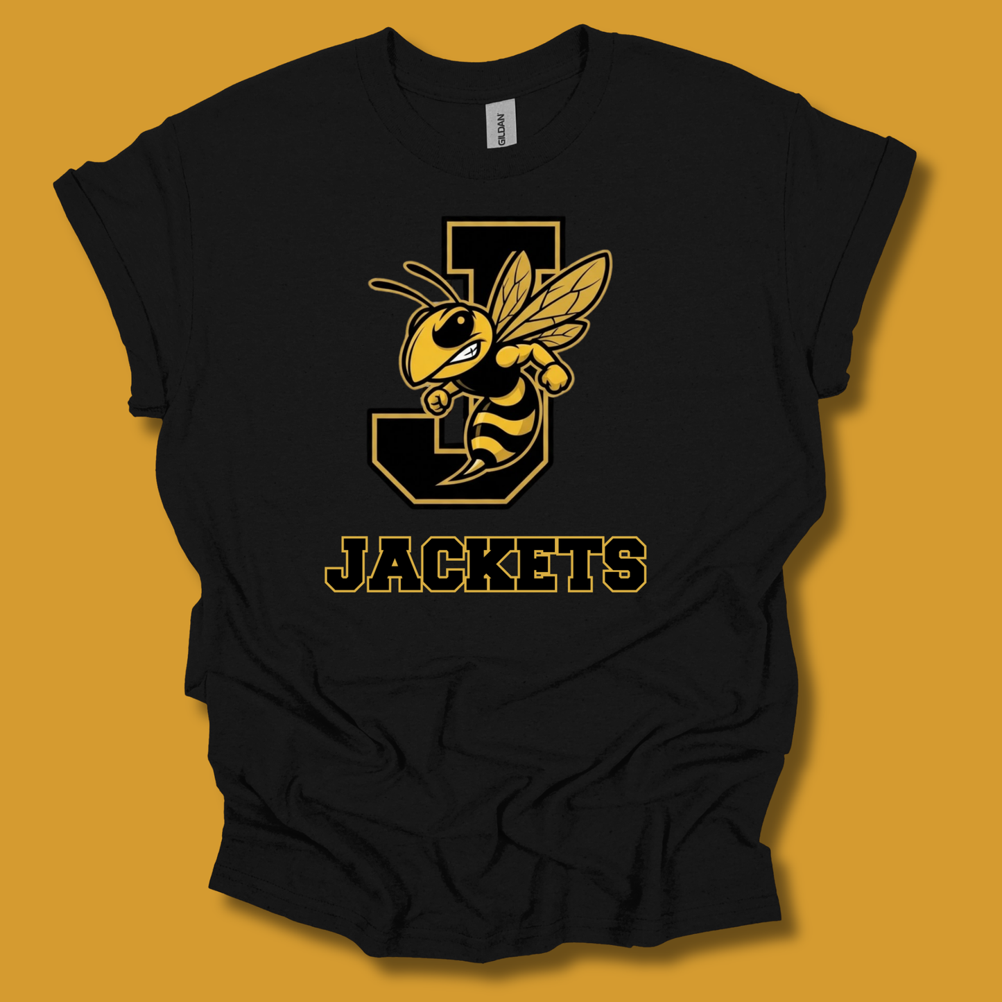 A black short-sleeve t-shirt with a yellow and black graphic of a bee mascot on a letter 'J' and the word 'JACKETS' printed below, displayed against a solid mustard yellow background.