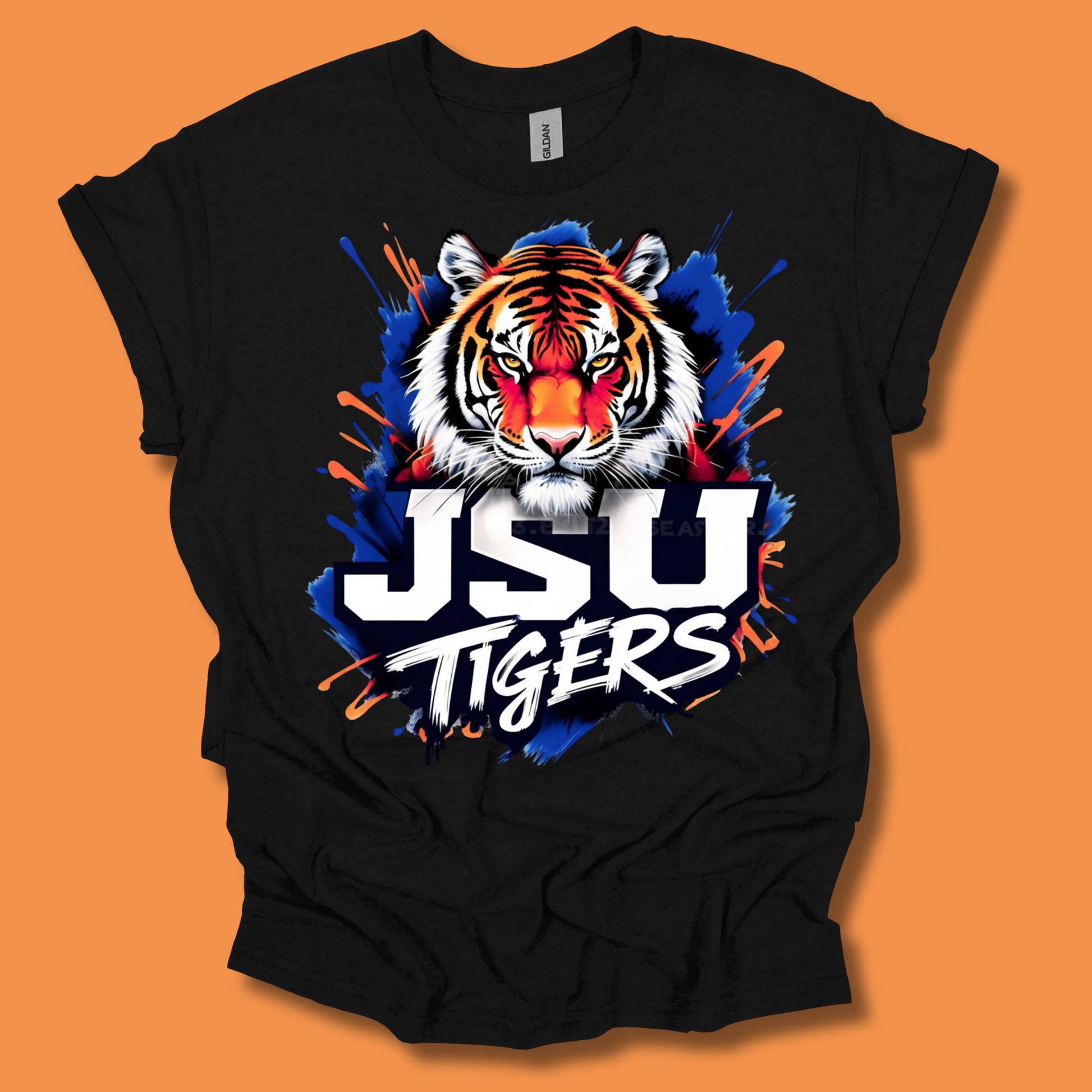 A black short-sleeve t-shirt with a vibrant graphic of a tiger's face and the text 'JSU TIGERS' over a blue paint splatter design, displayed on an orange background.