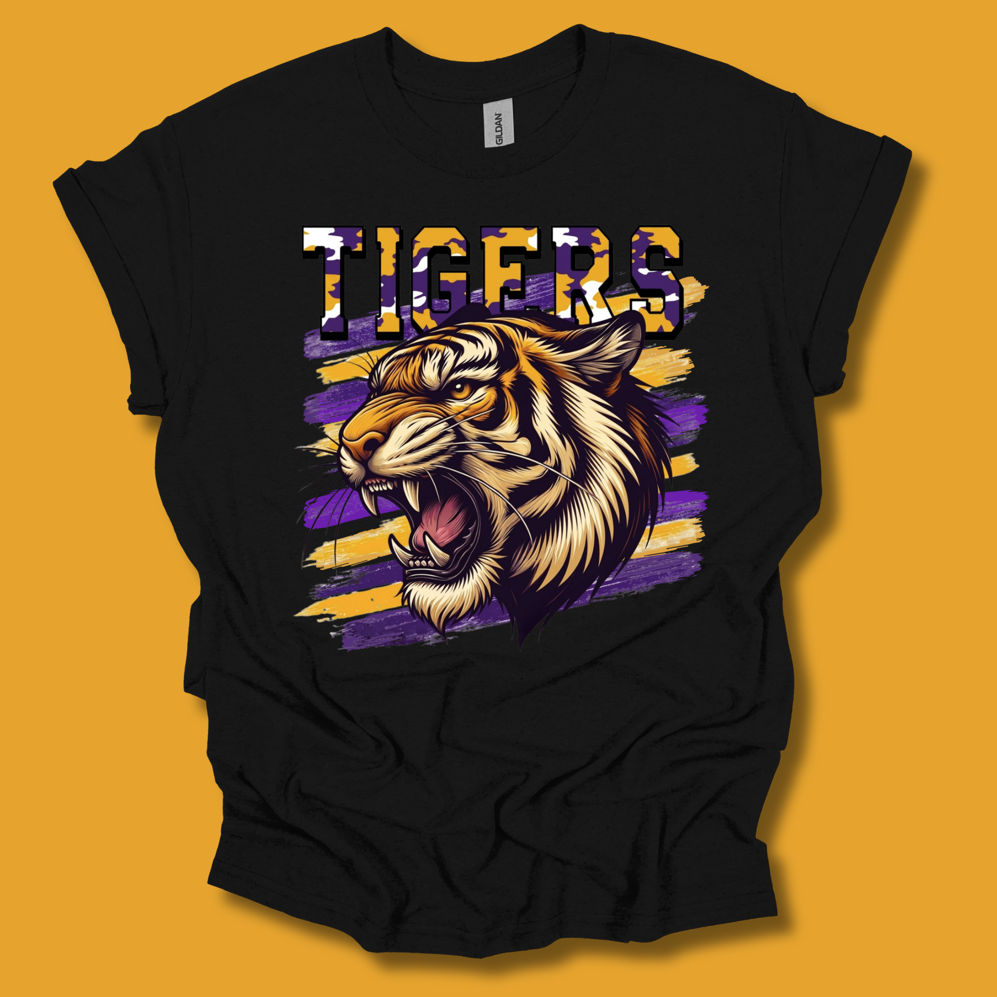 A black short-sleeve t-shirt with a graphic of a roaring tiger and the word 'TIGERS' in a purple, gold, and white patterned font, displayed against a solid mustard yellow background.