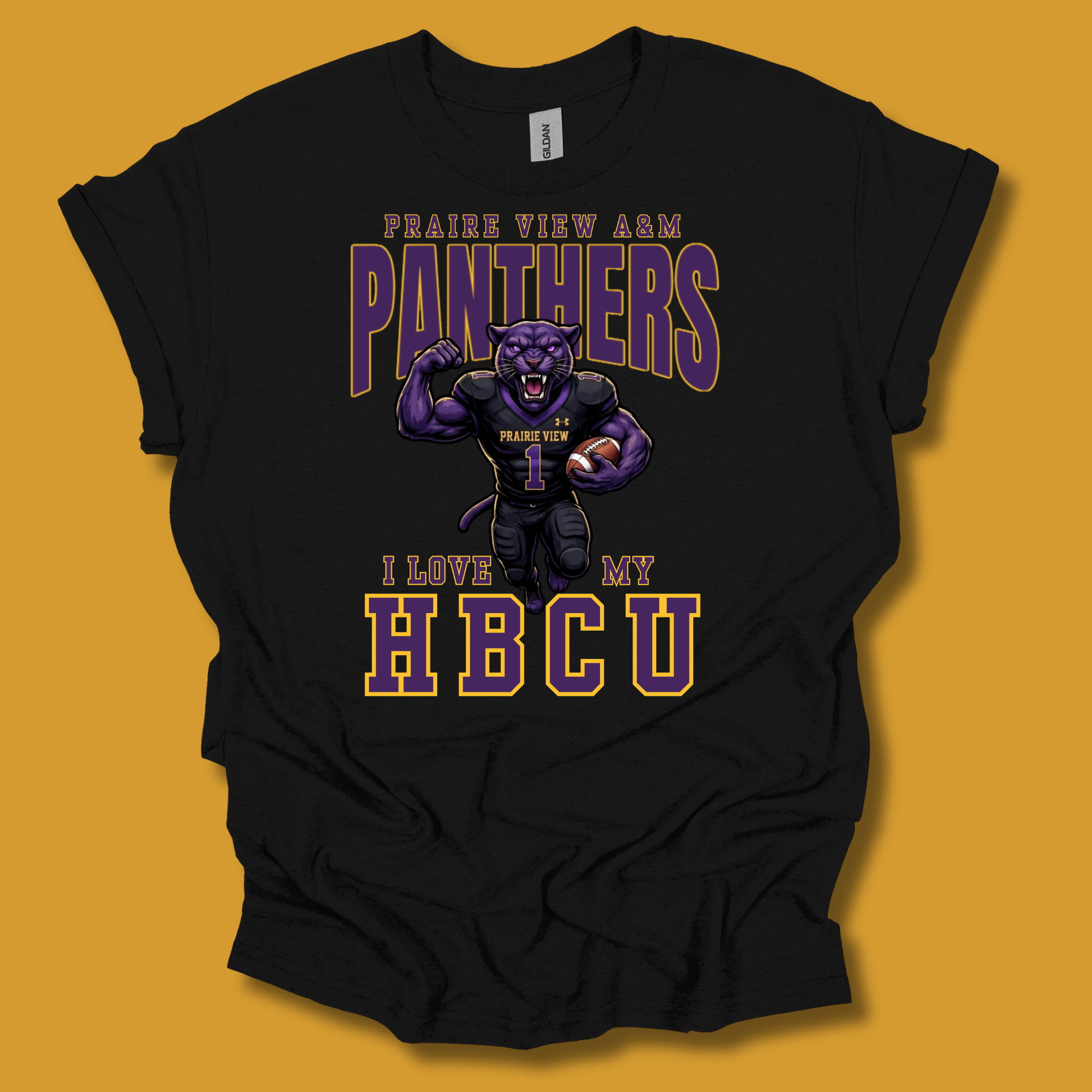 A black short-sleeve graphic t-shirt featuring a purple and gold design with the text 'PRAIRIE VIEW A&M PANTHERS I LOVE MY HBCU' and an illustration of a panther mascot, shown against a solid mustard yellow background.