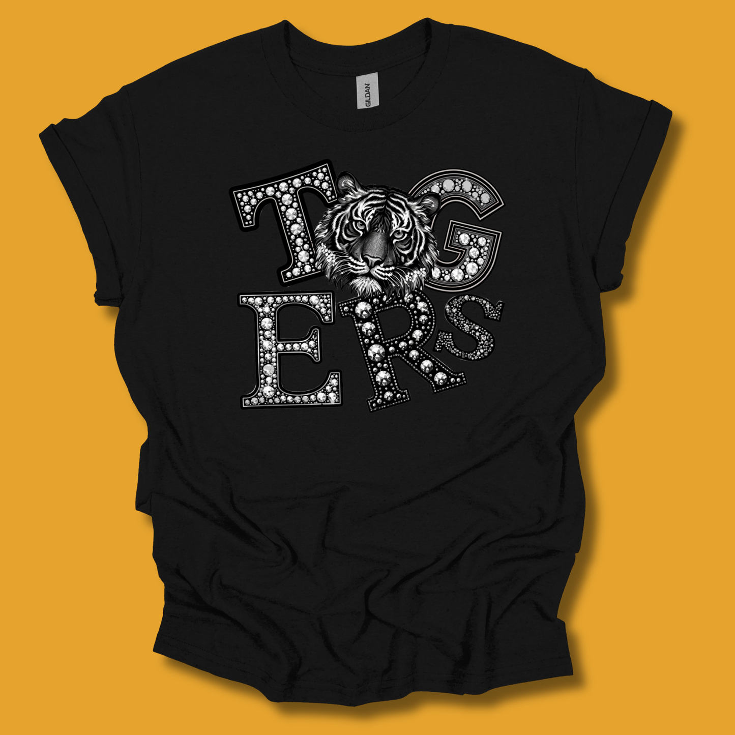 A black short-sleeve t-shirt with a graphic reading 'Tigers' in white letters filled with small rhinestones, featuring a tiger face in the center, displayed against a solid orange background.