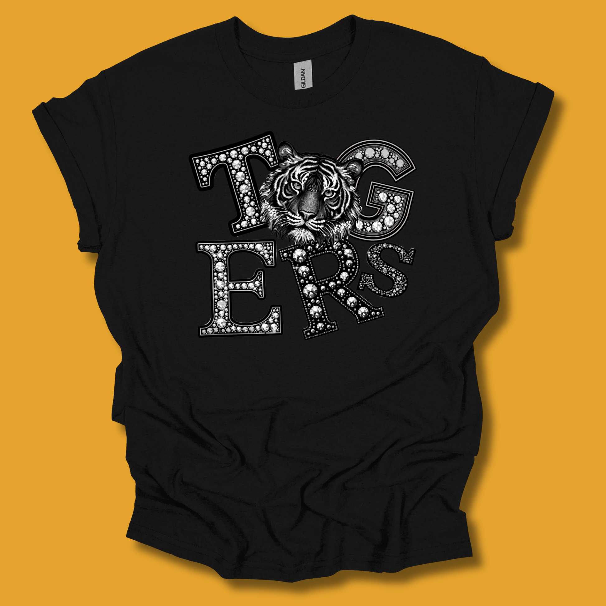 A black short-sleeve t-shirt with a graphic reading 'Tigers' in white letters filled with small rhinestones, featuring a tiger face in the center, displayed against a solid orange background.