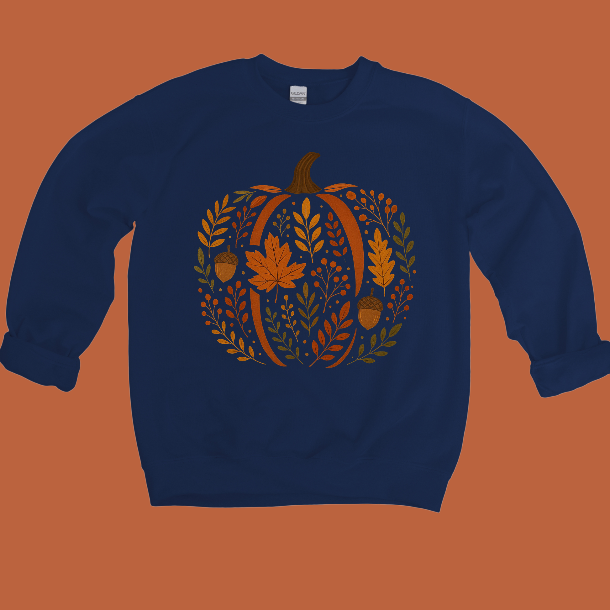 A navy blue crewneck sweatshirt featuring a large autumn-themed graphic of a pumpkin made of leaves, acorns, and a maple leaf, displayed against a solid orange background.
