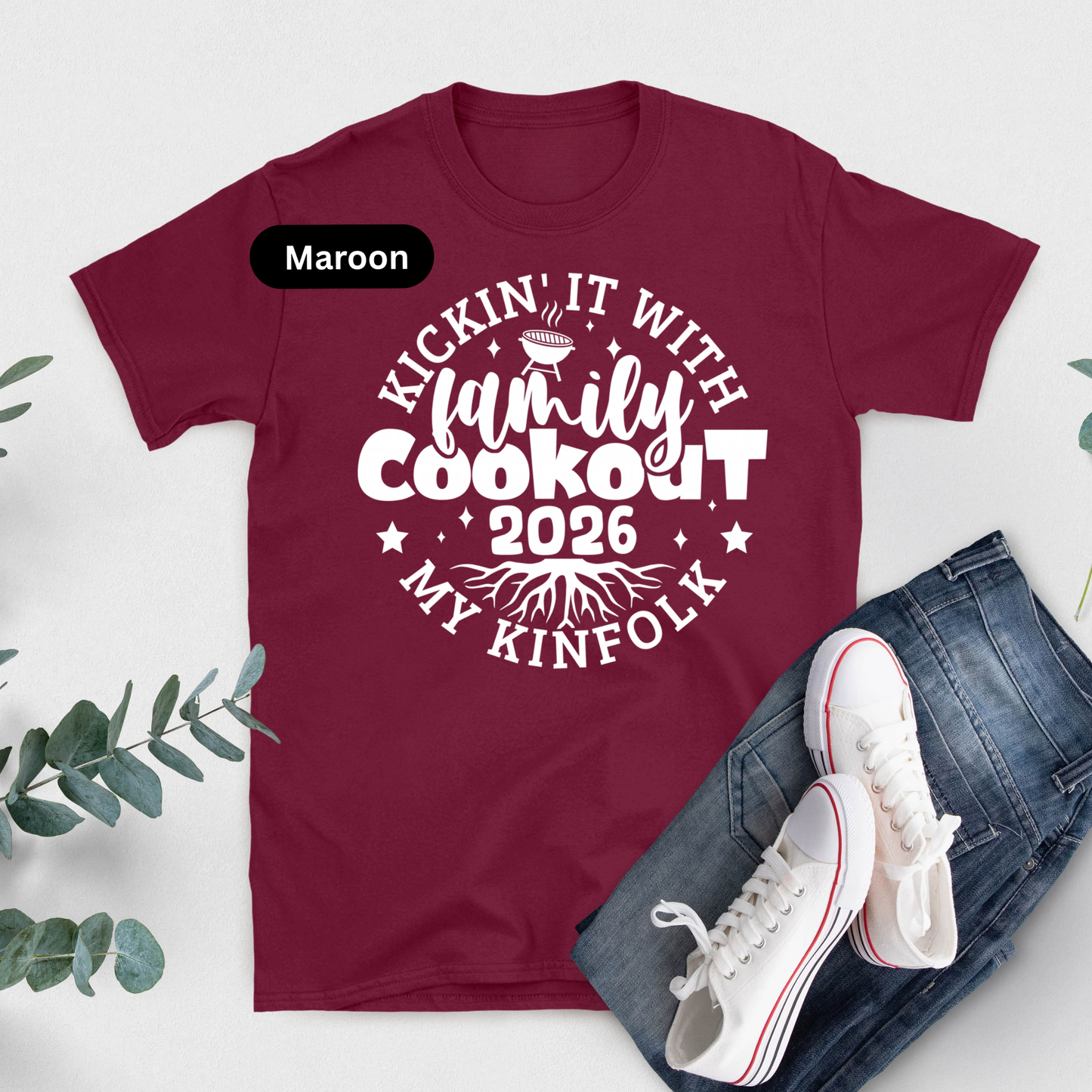 Maroon t-shirt with white text 'Kickin' it with family cookout 2026 my kinfolk' on a light gray background with jeans and sneakers.
