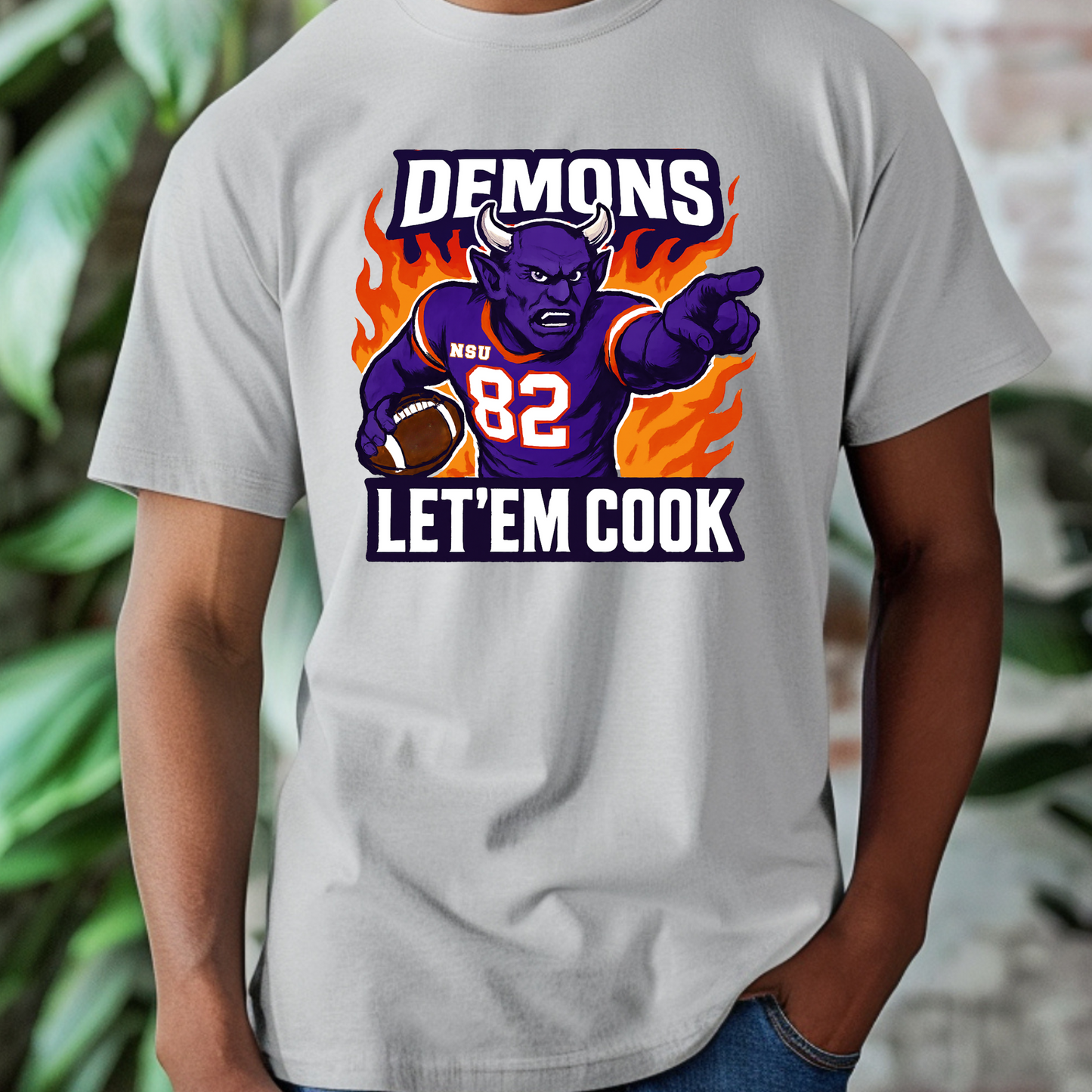 Gray t-shirt with a graphic of a demon holding a football and text 'DEMONS 82 LET'EM COOK' on a blurred background. Northwestern Demons Game Day T-Shirt - Demons  "Let'em Cook"  Football Tee