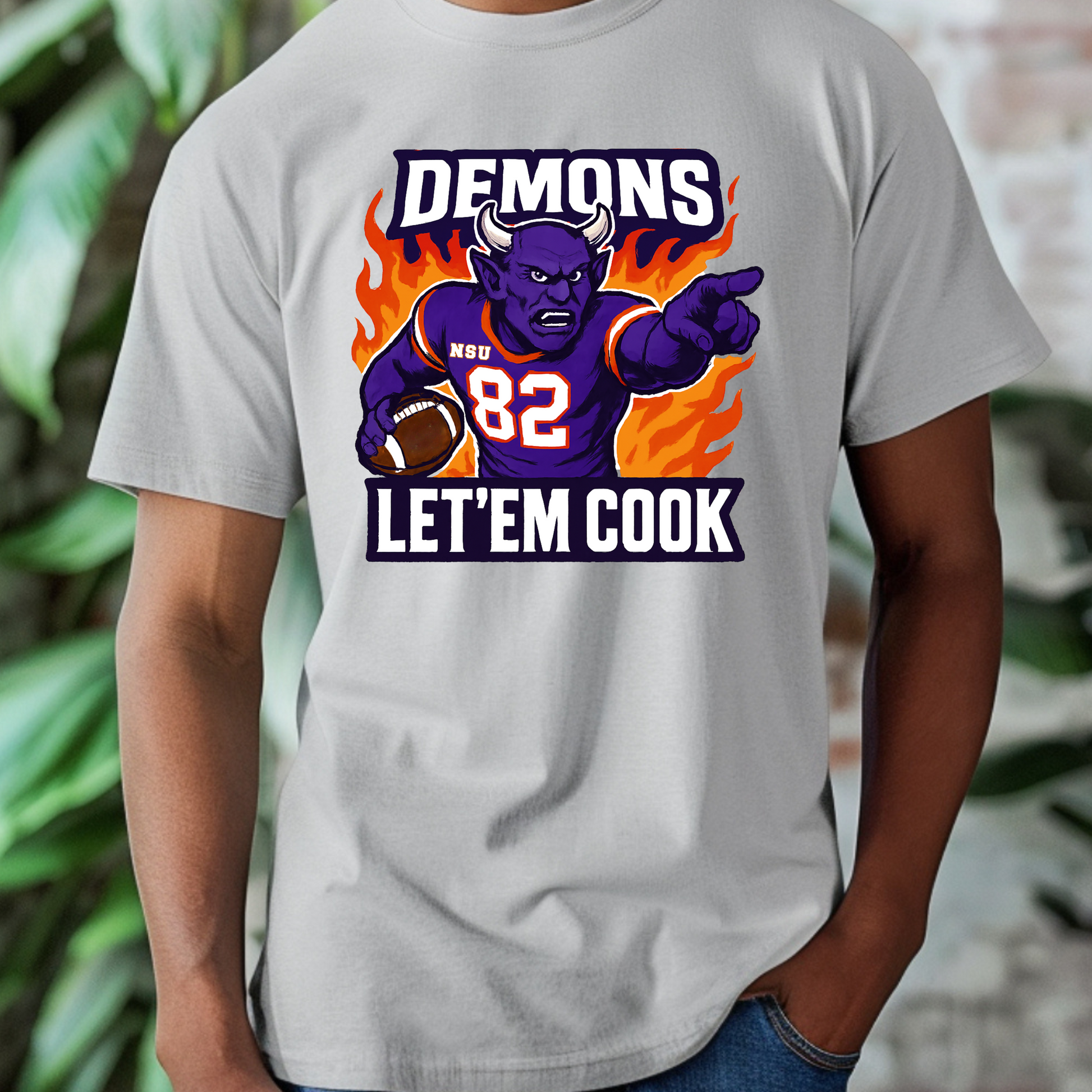 Gray t-shirt with a graphic of a demon holding a football and text 'DEMONS 82 LET'EM COOK' on a blurred background. Northwestern Demons Game Day T-Shirt - Demons  "Let'em Cook"  Football Tee