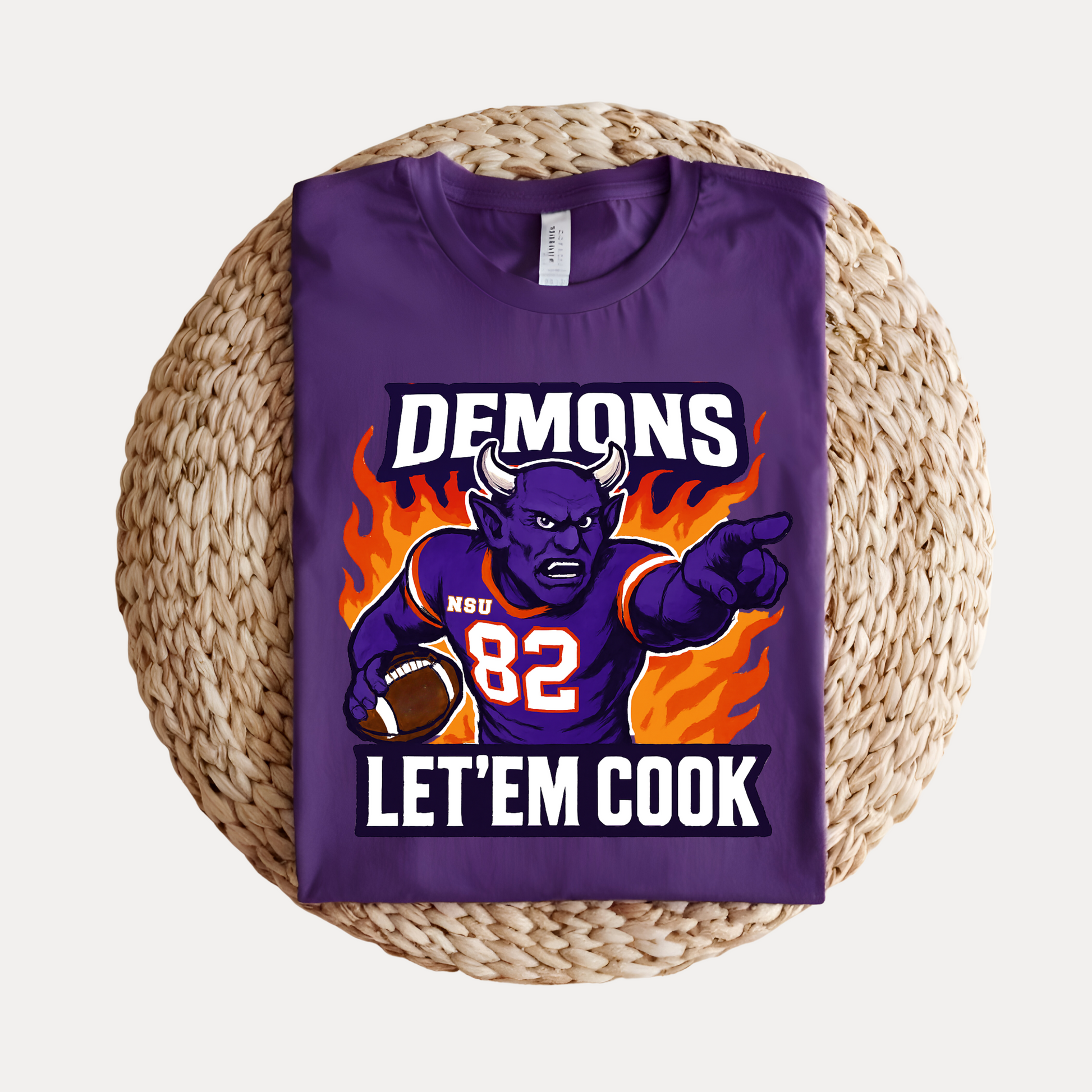 Purple t-shirt with a graphic design of a demon holding a football, text 'DEMONS 82 LET'EM COOK', on a woven mat. Northwestern Demons Game Day T-Shirt - Demons  "Let'em Cook"  Football Tee