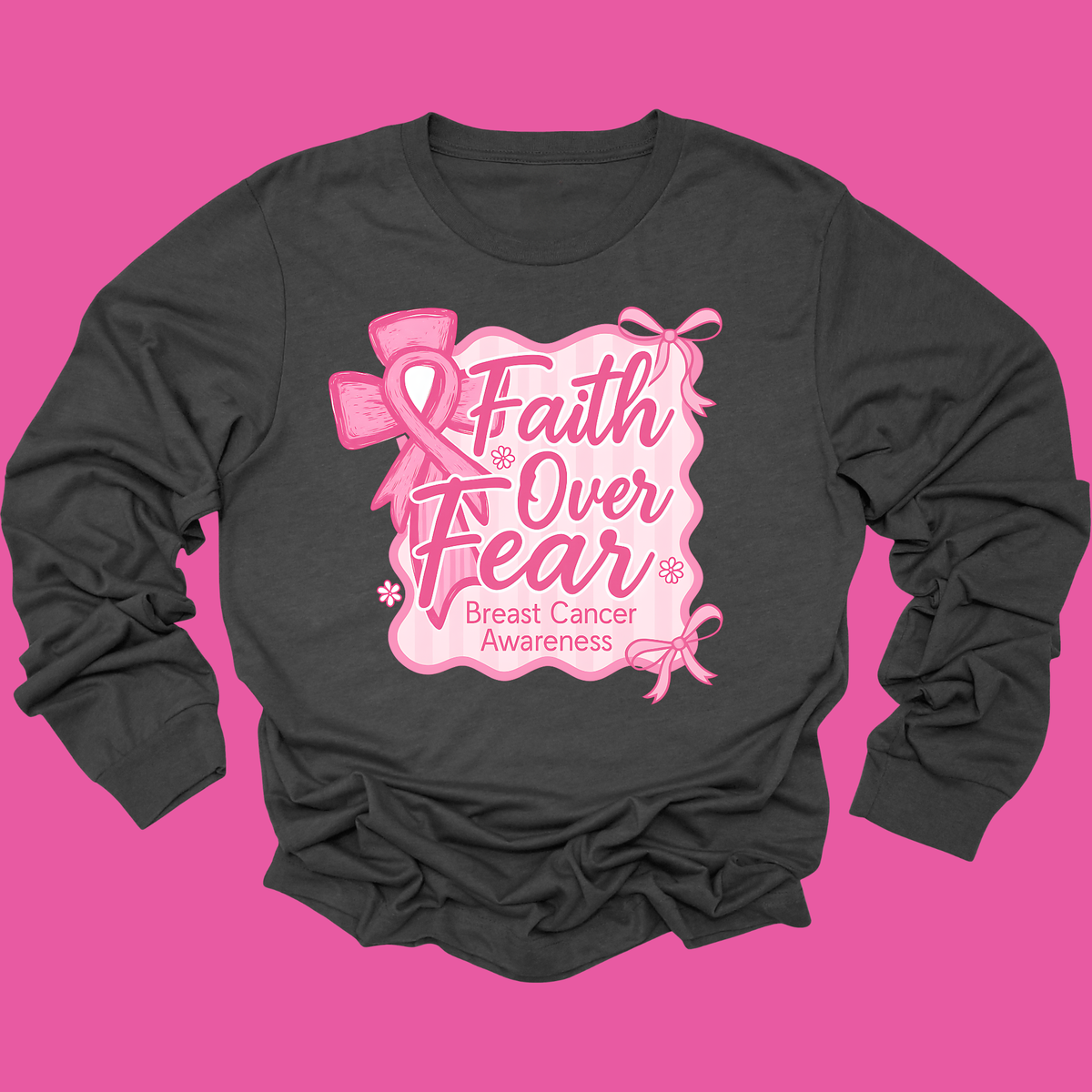 A dark charcoal gray long-sleeve t-shirt with a pink graphic on the front that reads 'Faith Over Fear Breast Cancer Awareness' with pink ribbon illustrations, displayed against a solid pink background.