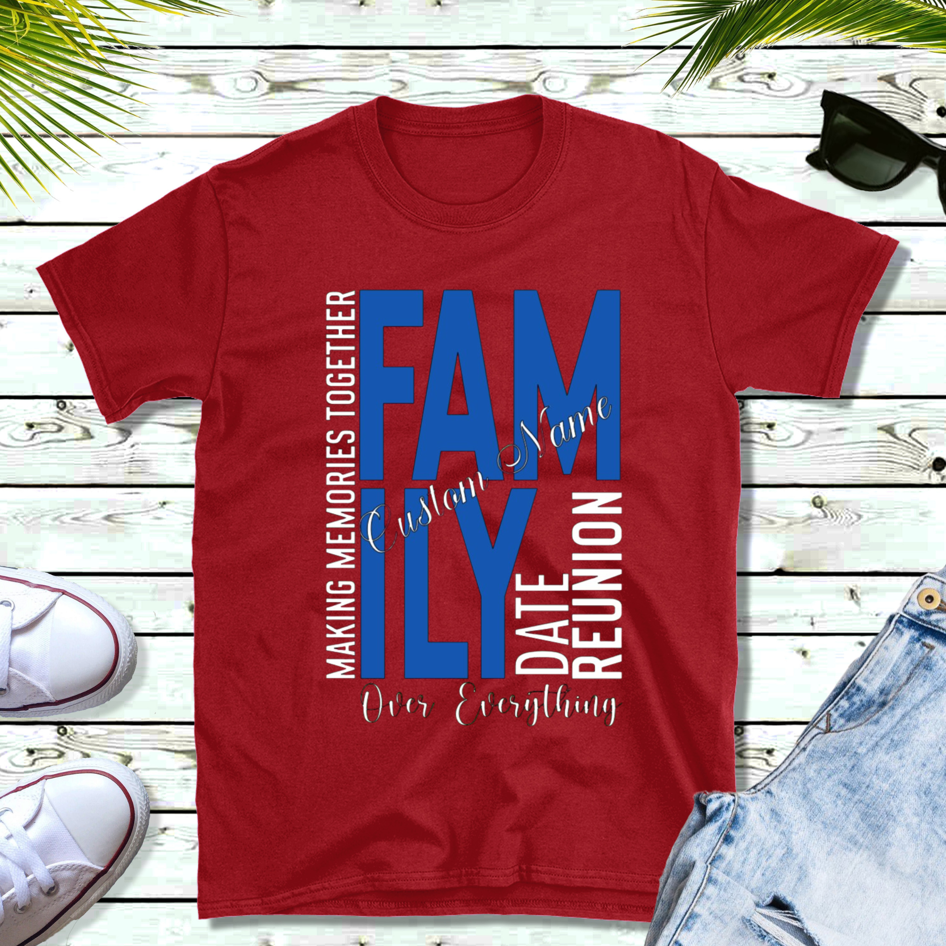 Red t-shirt with blue and white text on a wooden surface with shoes and sunglasses.