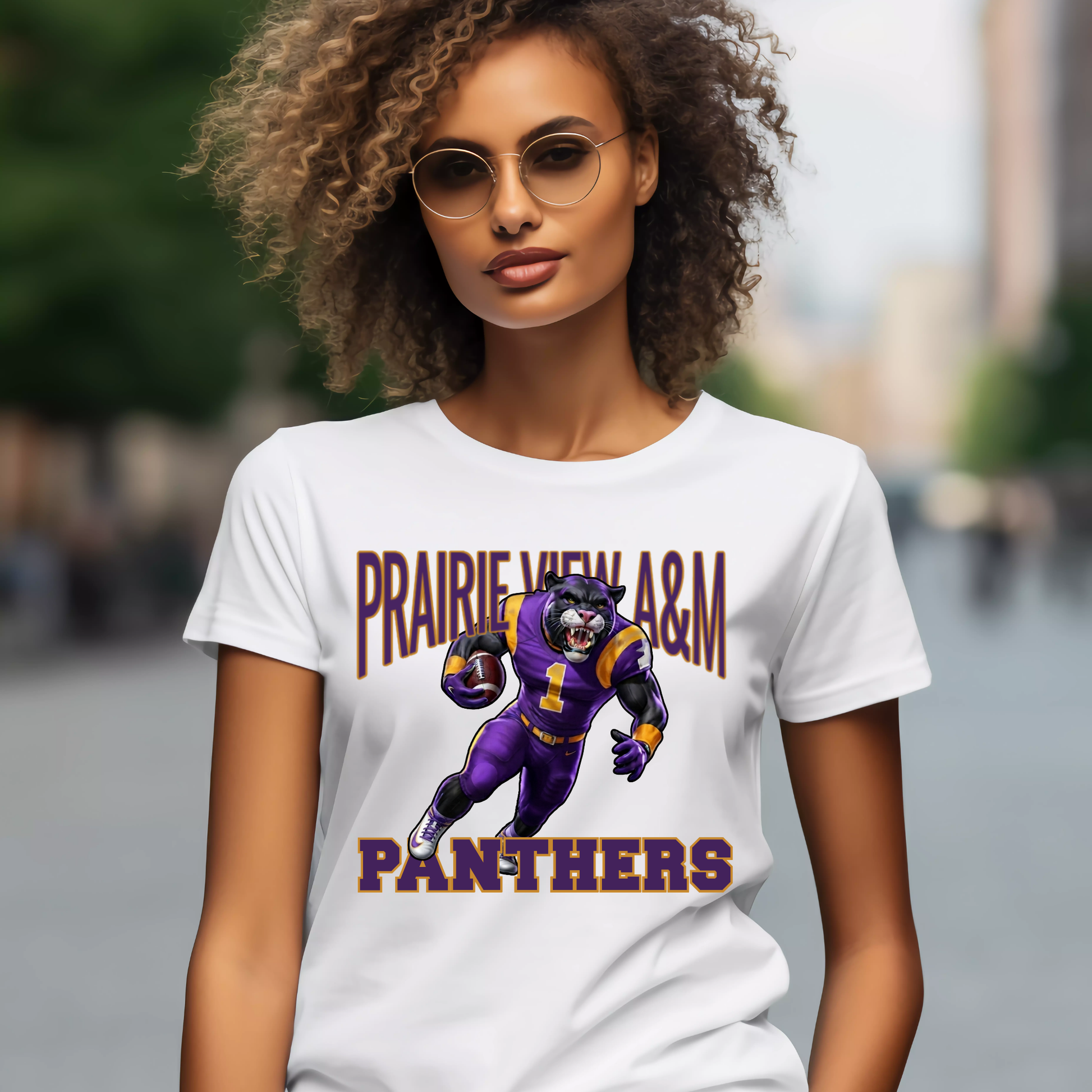 A woman wearing a white graphic t-shirt with a purple and gold 'Prairie View A&M Panthers' football player illustration, set against a blurred outdoor city background.