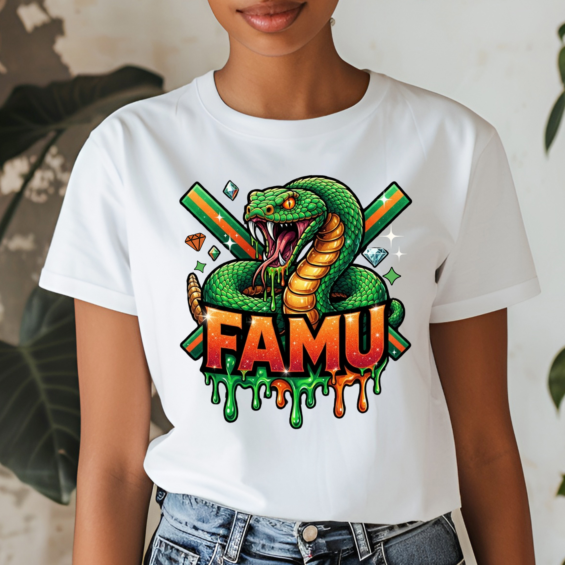 A person wearing a white short-sleeve graphic T-shirt with a colorful snake illustration and the word 'FAMU' on the front, paired with blue jeans in an indoor setting with plants in the background.
