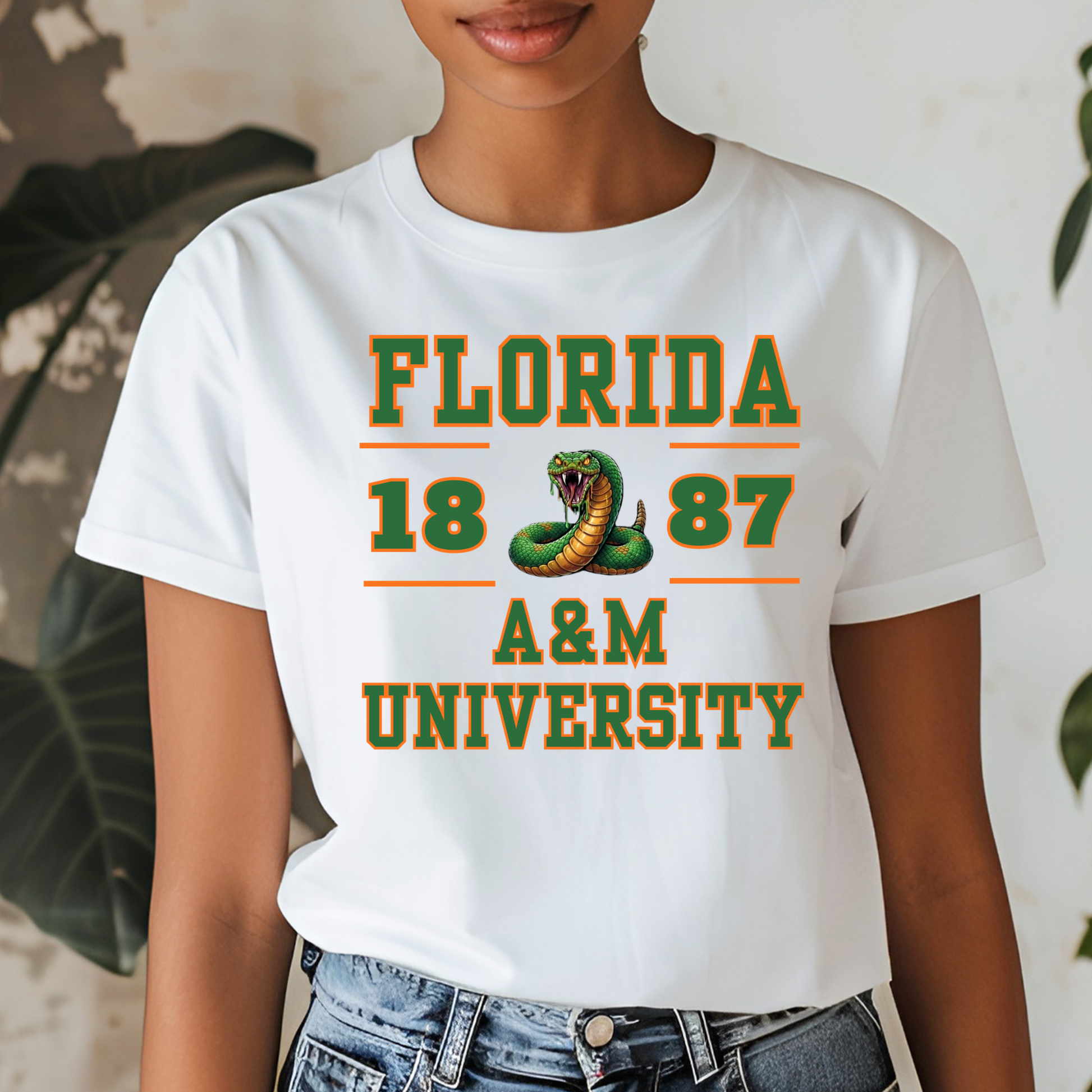 A woman wearing a white graphic t-shirt with 'FLORIDA 1887 A&M UNIVERSITY' printed in green and orange, featuring a snake graphic, paired with blue jeans.