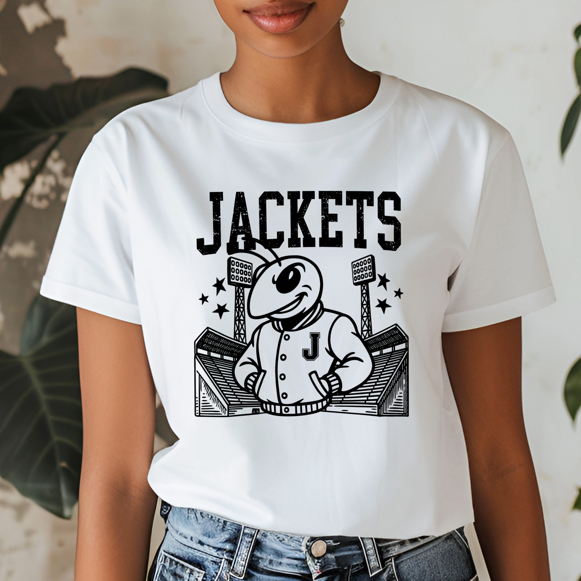 A woman wearing a white short-sleeve graphic T-shirt with a black cartoon mascot and the word 'JACKETS' printed on the front, paired with blue jeans.