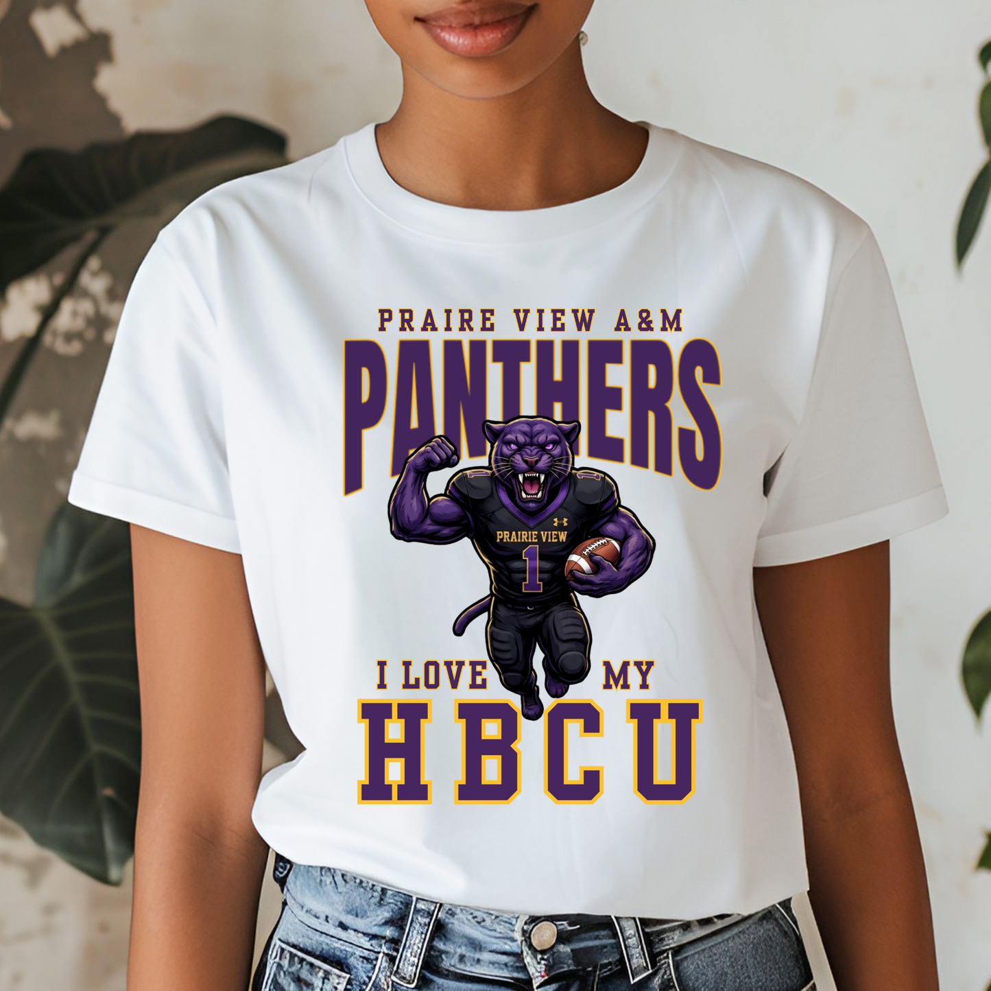 A woman wearing a white graphic t-shirt with a purple and gold print that reads 'PRAIRE VIEW A&M PANTHERS I LOVE MY HBCU' with an illustration of a running panther football player.
