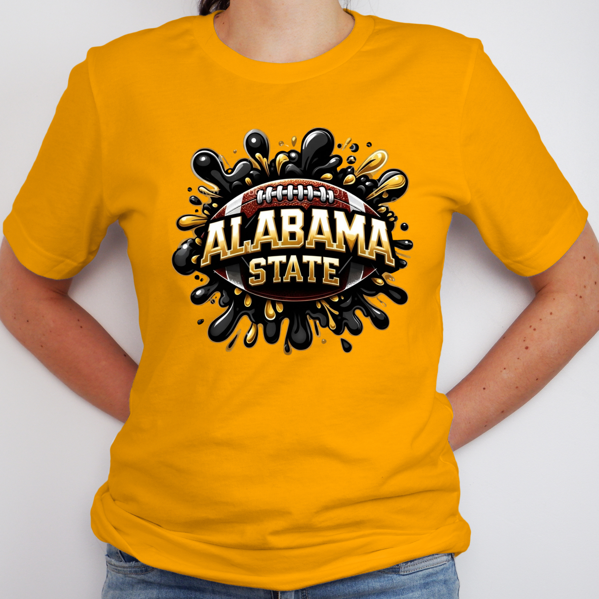 A person wearing a bright yellow short-sleeve t-shirt with a graphic on the chest. The graphic features a football surrounded by black paint splatters and the words 'ALABAMA STATE' in gold and white.
