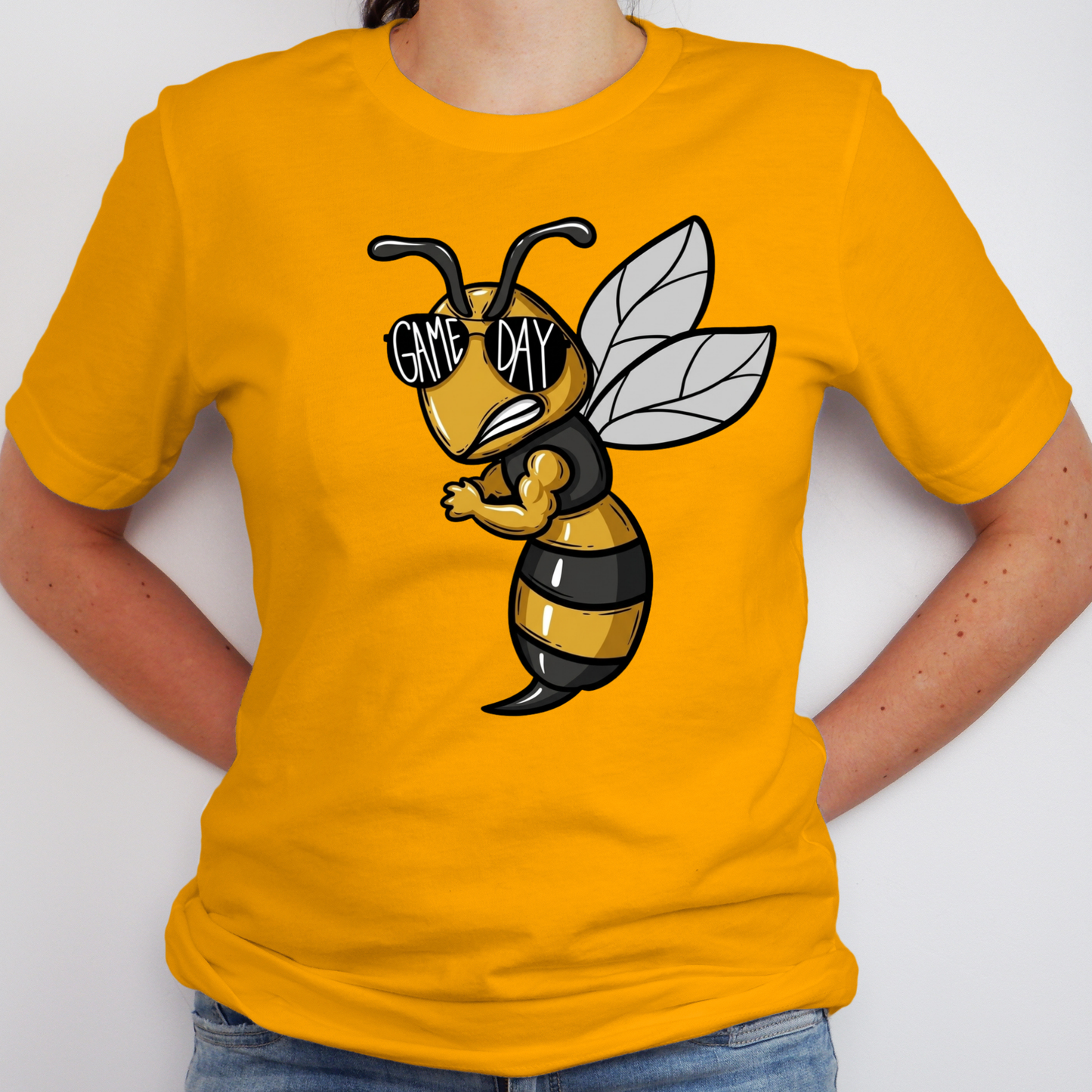 A person wearing a bright yellow t-shirt with a cartoon bee graphic on the chest. The bee is black and yellow with white wings and black sunglasses that read 'GAME DAY'.