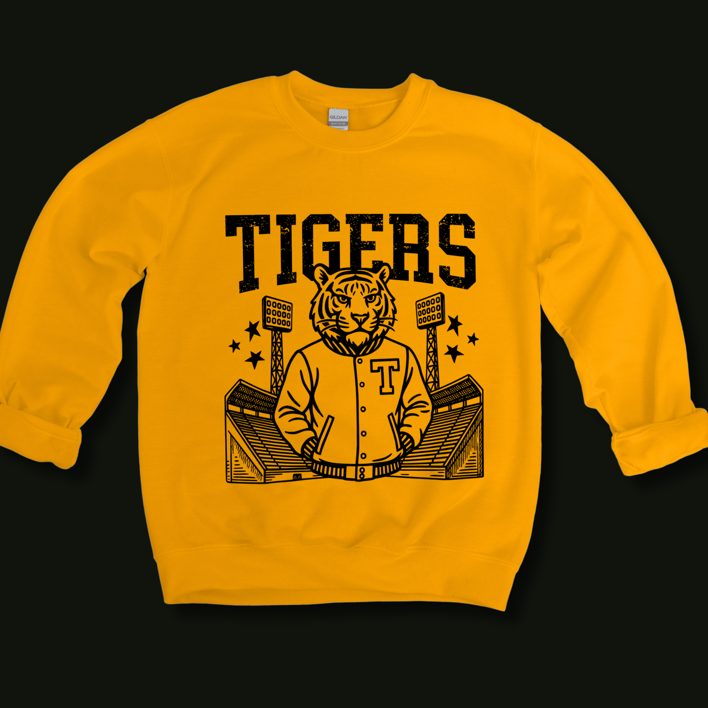 A yellow crewneck sweatshirt with a black graphic print of a tiger mascot in a varsity jacket, stadium lights, and the word 'TIGERS' above, shown against a solid black background.