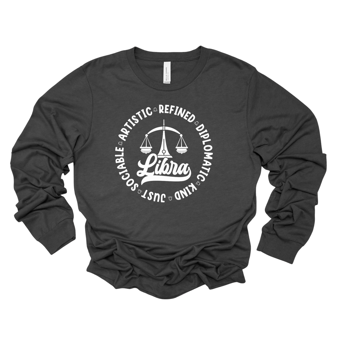 Woman wearing a white crewneck t-shirt featuring a black circular Libra zodiac graphic with a scales illustration, the word "Libra," and trait keywords like artistic, refined, diplomatic, kind, just, and sociable.