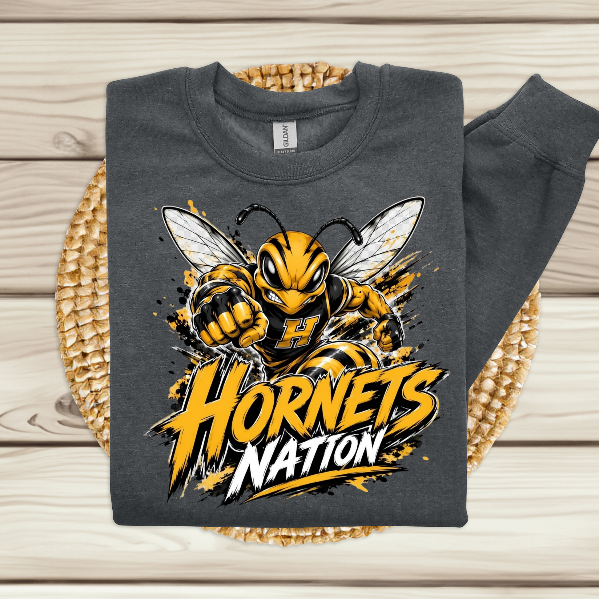 A dark gray sweatshirt laid flat on a woven round mat over a light wood plank surface. The sweatshirt features a large graphic of a yellow and black hornet mascot with the text 'Hornets Nation' in bold yellow and white lettering.