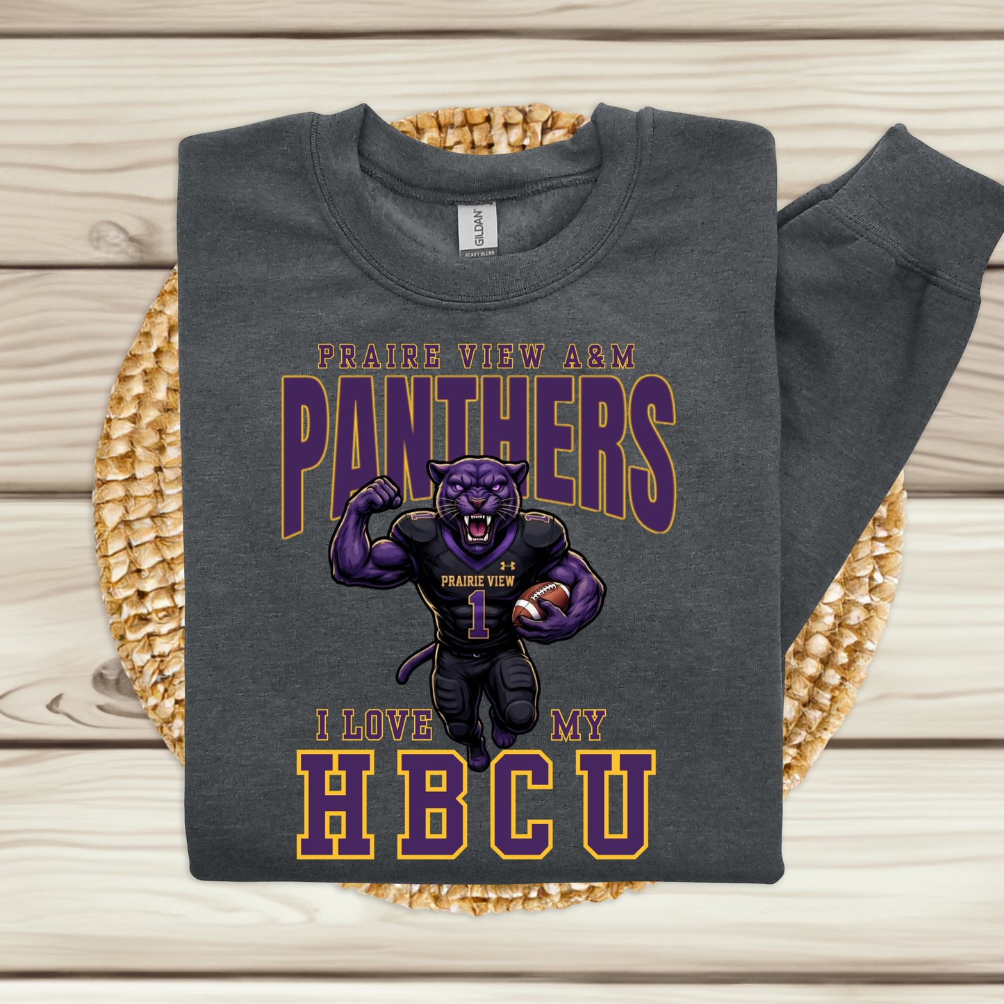 A dark gray sweatshirt with a 'Prairie View A&M Panthers' graphic, displayed flat on a woven placemat over a light wood background.