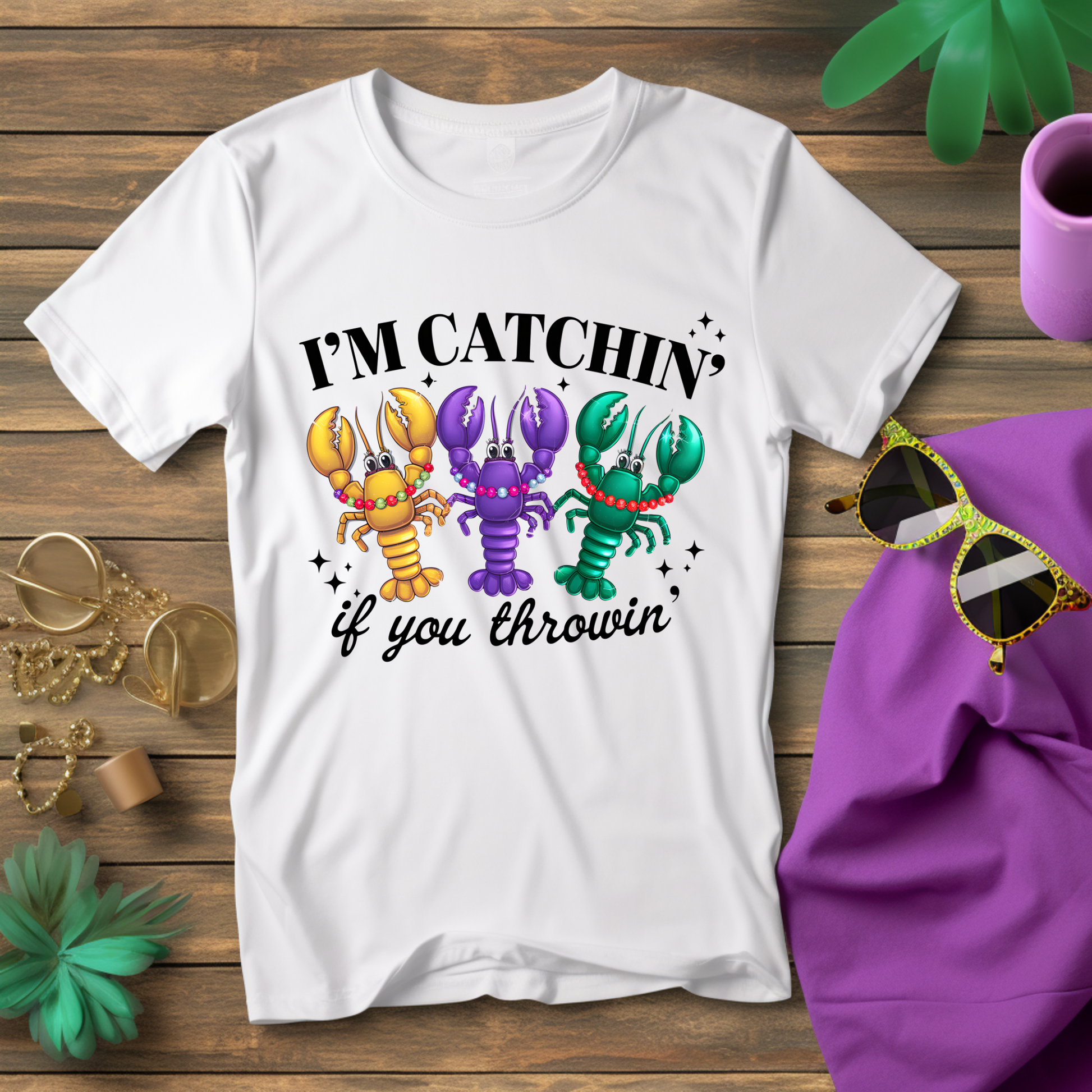 White t-shirt with colorful lobster graphic and text on a wooden surface with accessories.
