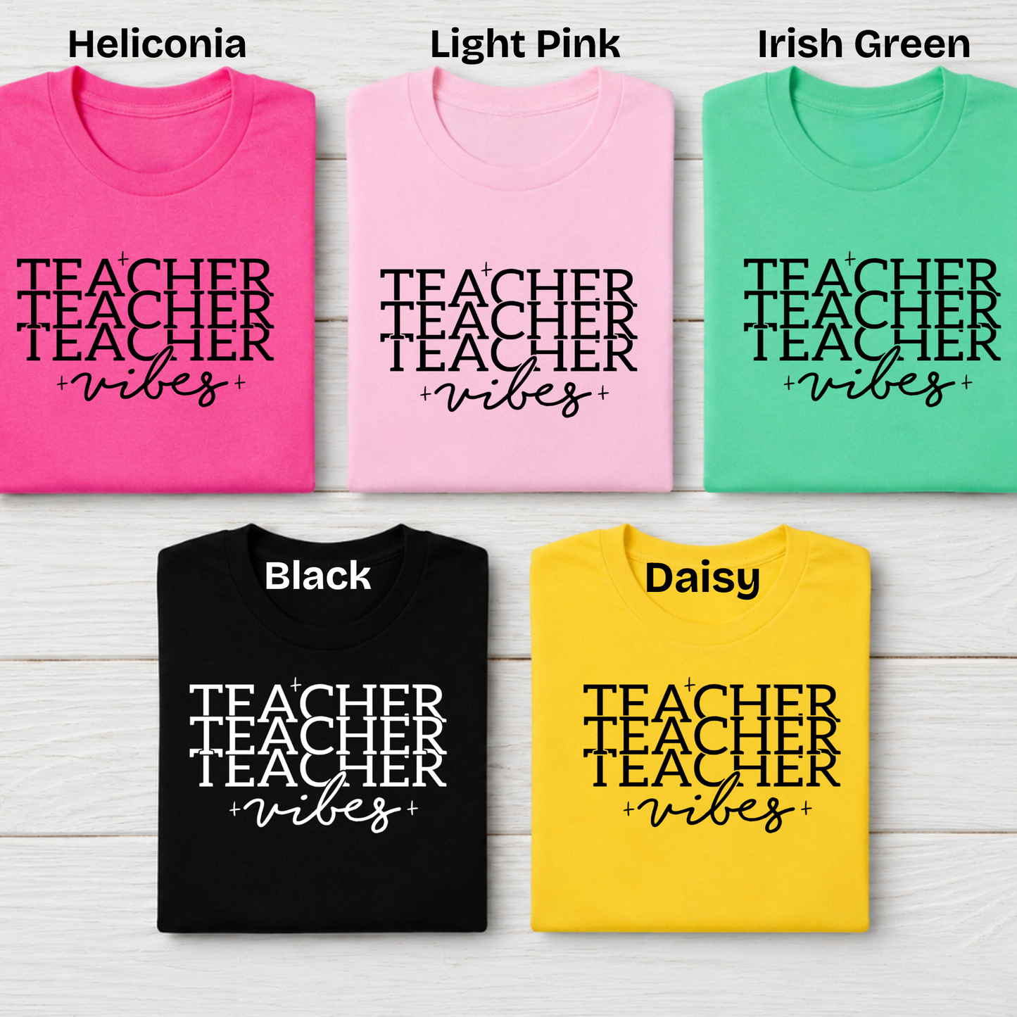 Five folded graphic T-shirts arranged in a 2x3 grid on a white wood background, labeled with color names at the top: Heliconia pink, Light Pink, Irish Green, Black, and Daisy yellow. Each shirt has the words 'TEACHER vibes' printed in large black script across the front.
